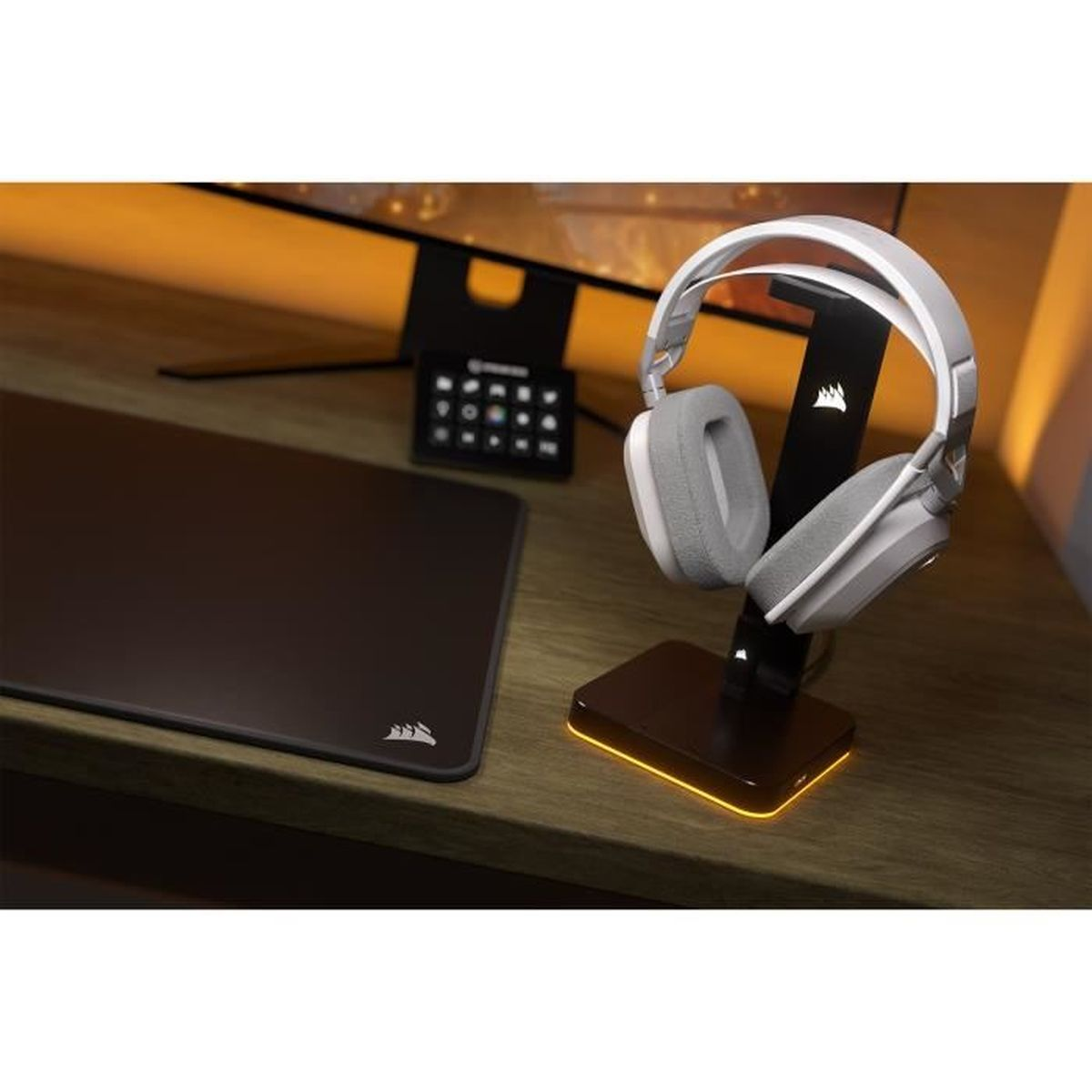 Słuchawki na stojaku, podkładka pod mysz i monitor na drewnianym biurku. Ciepłe oświetlenie.