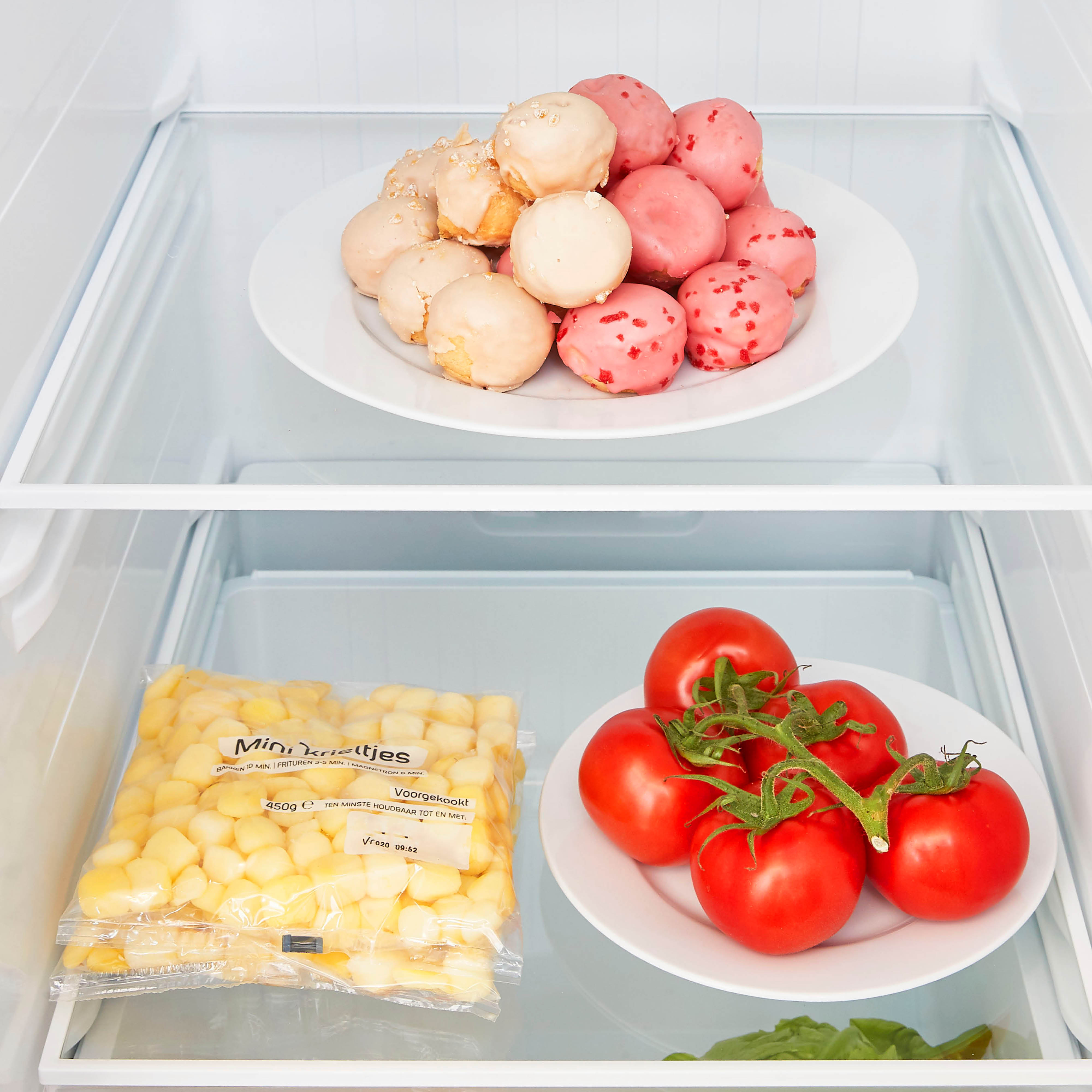 Refrigerator interior showing plates of donuts and tomatoes with corn.
