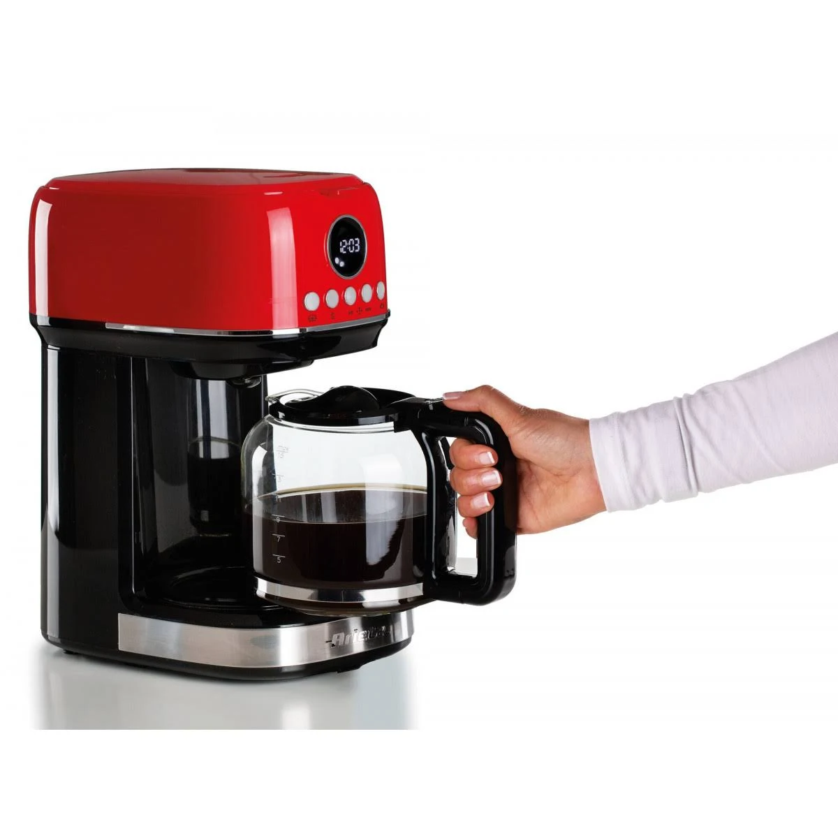 Cafetera roja y negra con jarra de vidrio. La mano de una persona sostiene la jarra.
