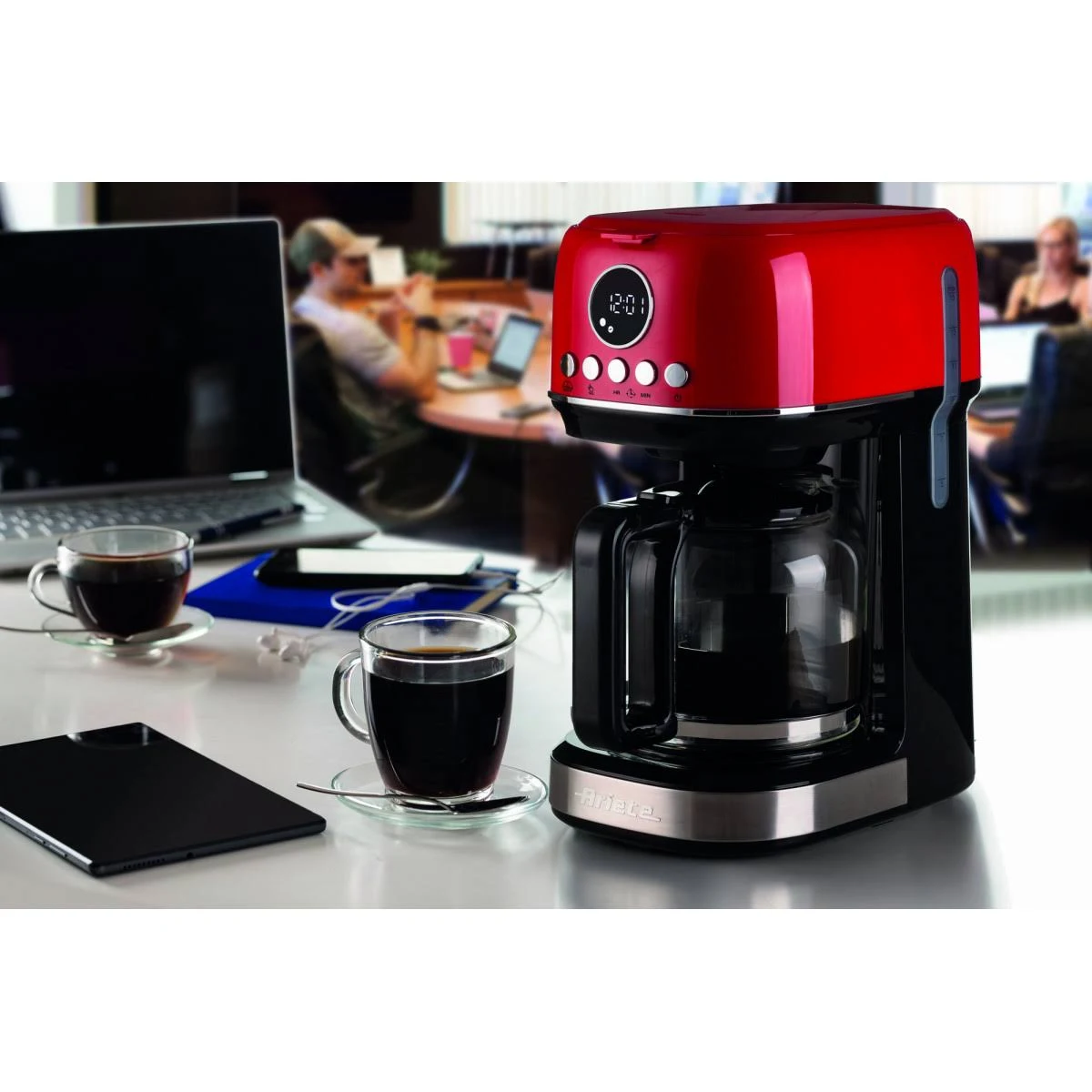 Una cafetera roja con una jarra de vidrio y dos tazas de café sobre una mesa.