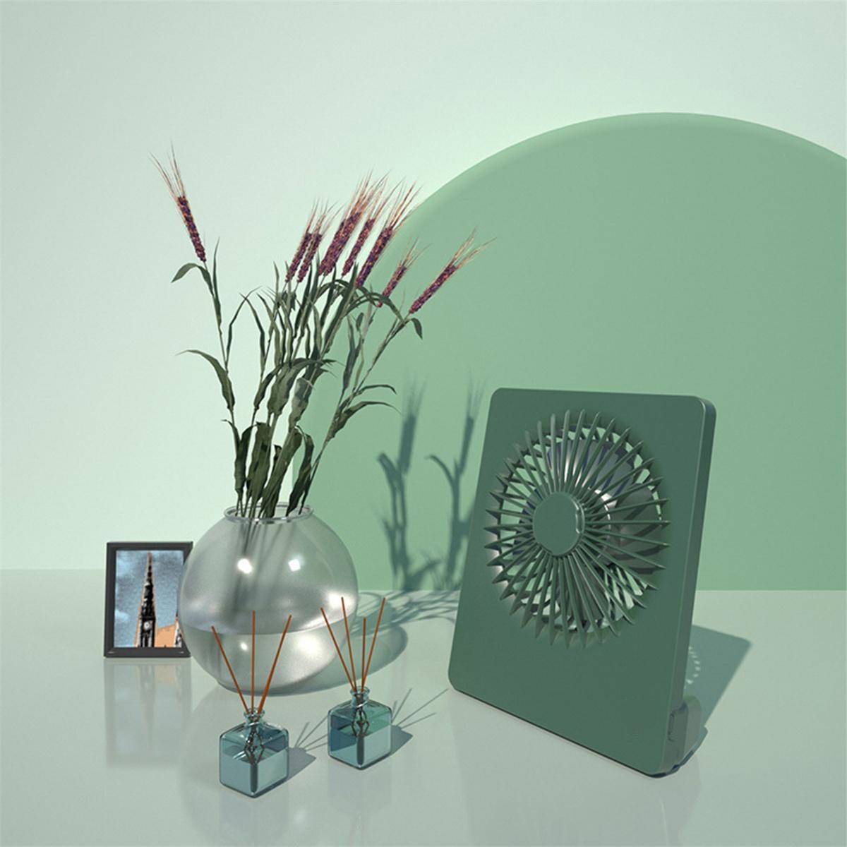 Ein grüner Ventilator und eine Vase mit Blumen und einigen anderen dekorativen Gegenständen auf einem Tisch. Grüner Hintergrund.