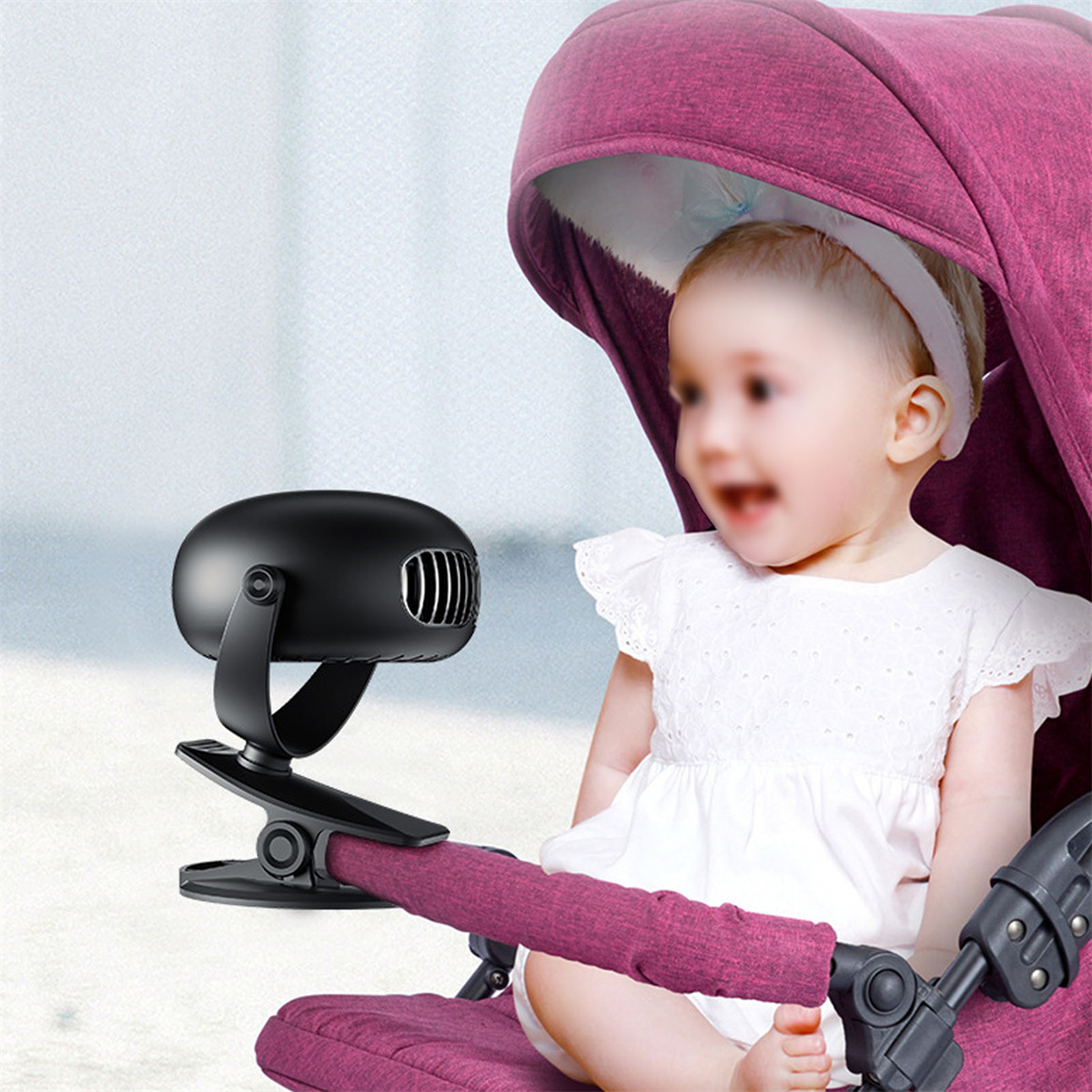 Ein Baby in einem Kinderwagen mit einem schwarzen Ventilator am Rahmen. Das Baby lächelt.