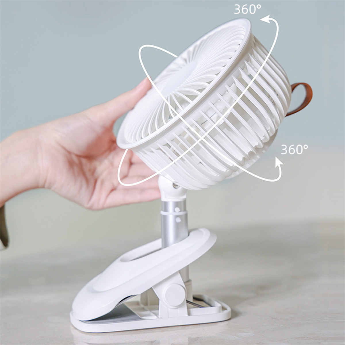 Ein weißer tragbarer Ventilator mit einstellbarer Richtung, und eine Hand in der Nähe.