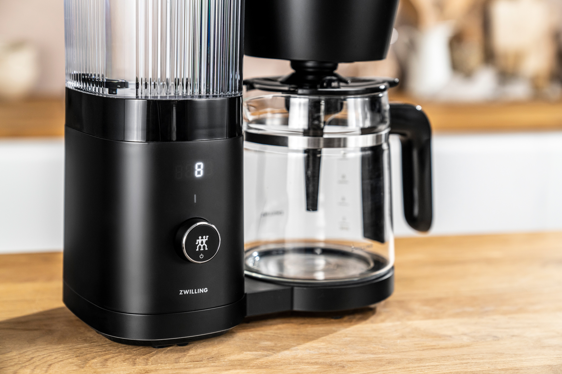 Una macchina da caffè nera con una caraffa di vetro, bancone di legno sullo sfondo.