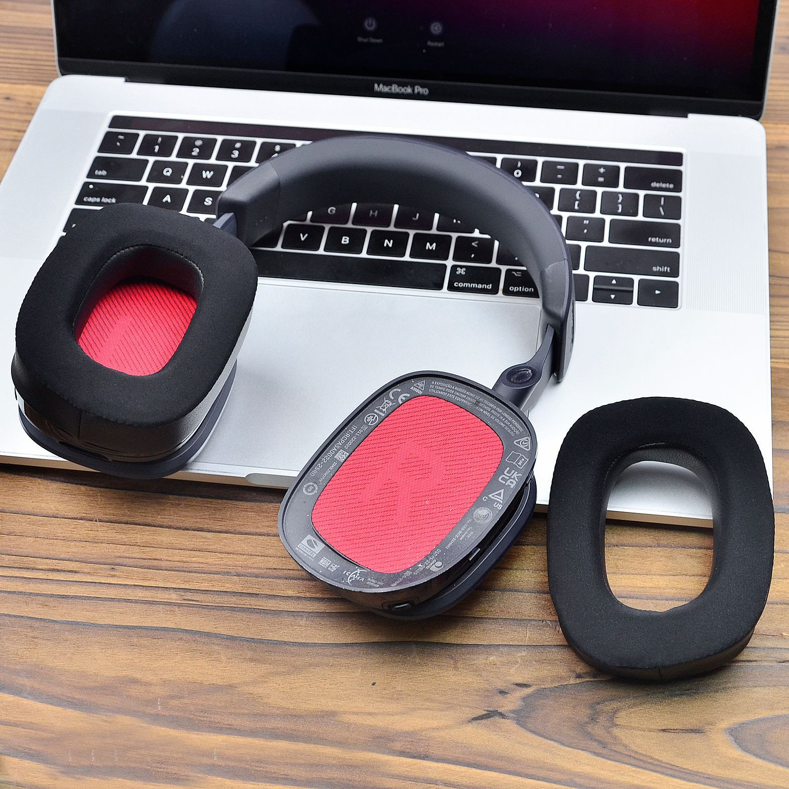 Kopfhörer auf einem Laptop. Schwarze Ohrmuscheln, rotes Innenleben. Holzoberfläche.