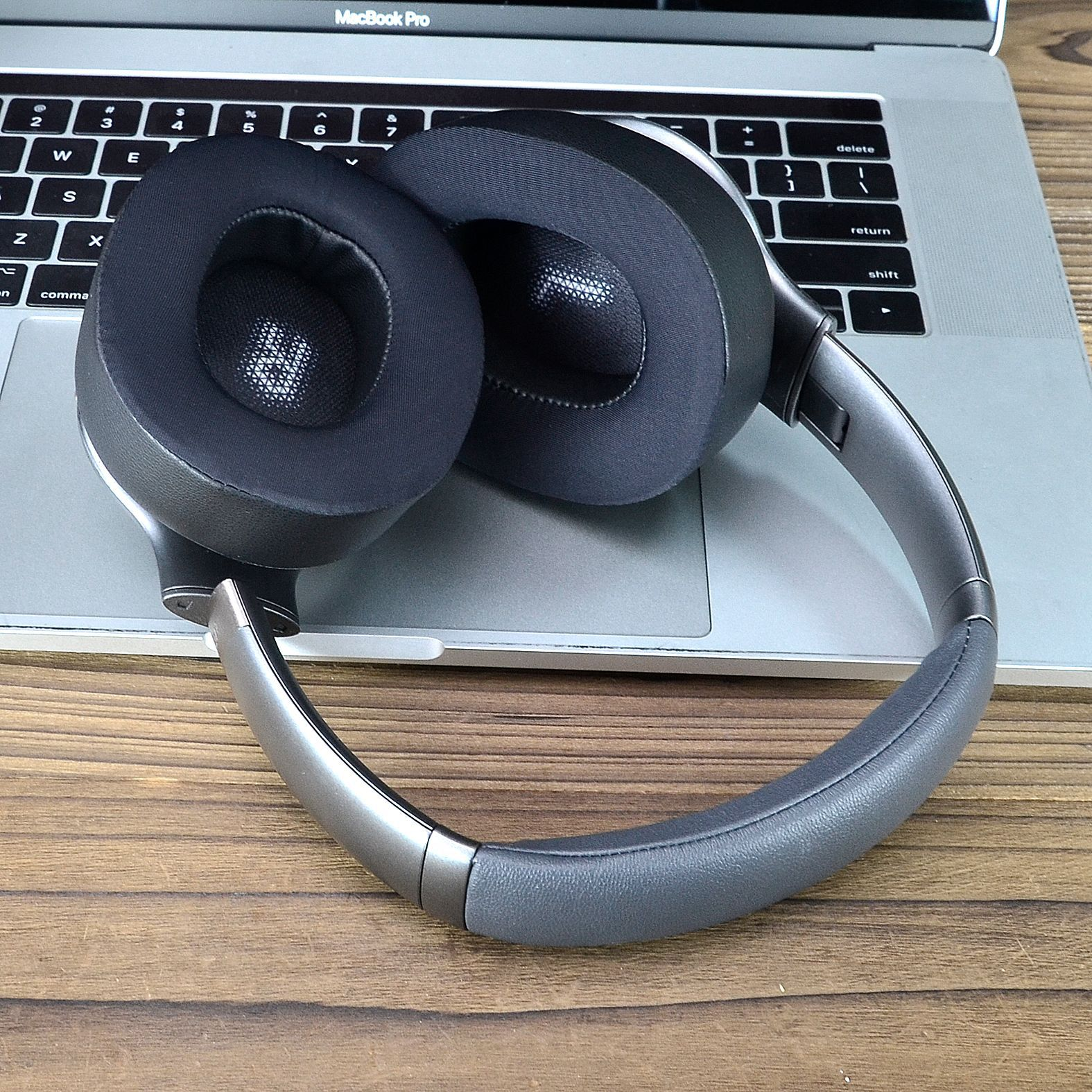 Over-Ear-Kopfhörer auf einem Laptop. Die Kopfhörer sind grau und schwarz, mit einem Holztisch als Hintergrund.