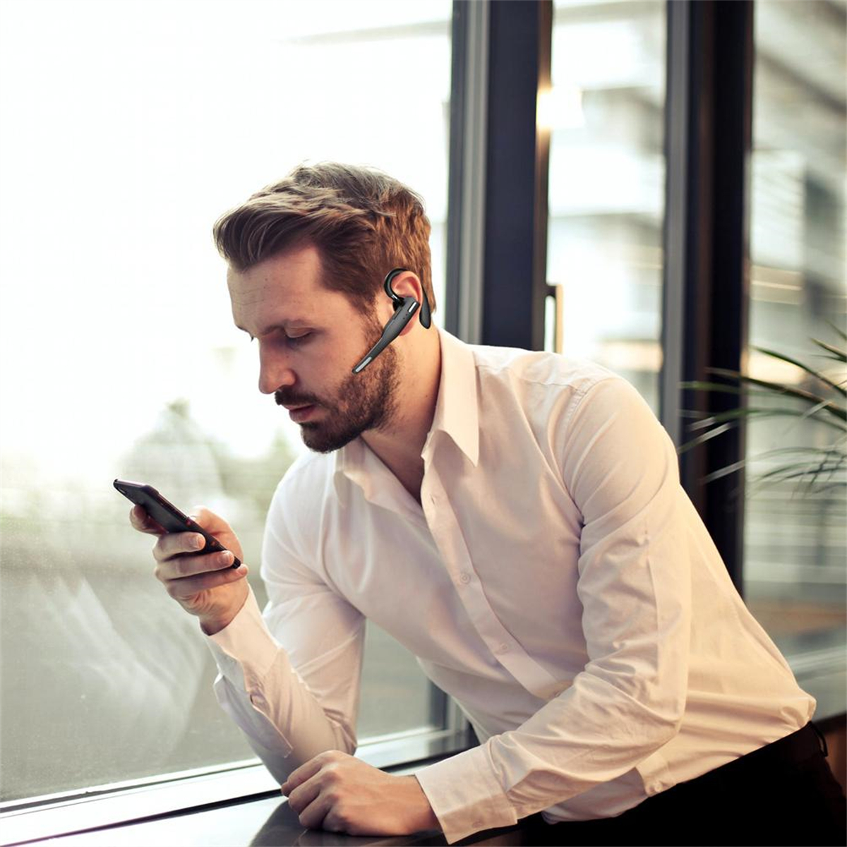 Mann, der ein Headset und Telefon in der Nähe eines Fensters benutzt.