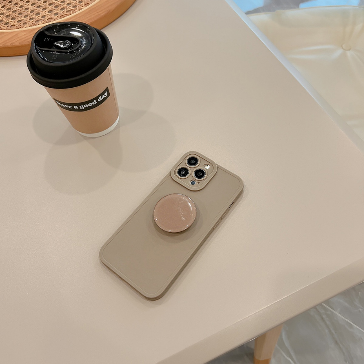 Handyhülle mit Pop-Socket und Kaffeetasse auf heller Oberfläche.