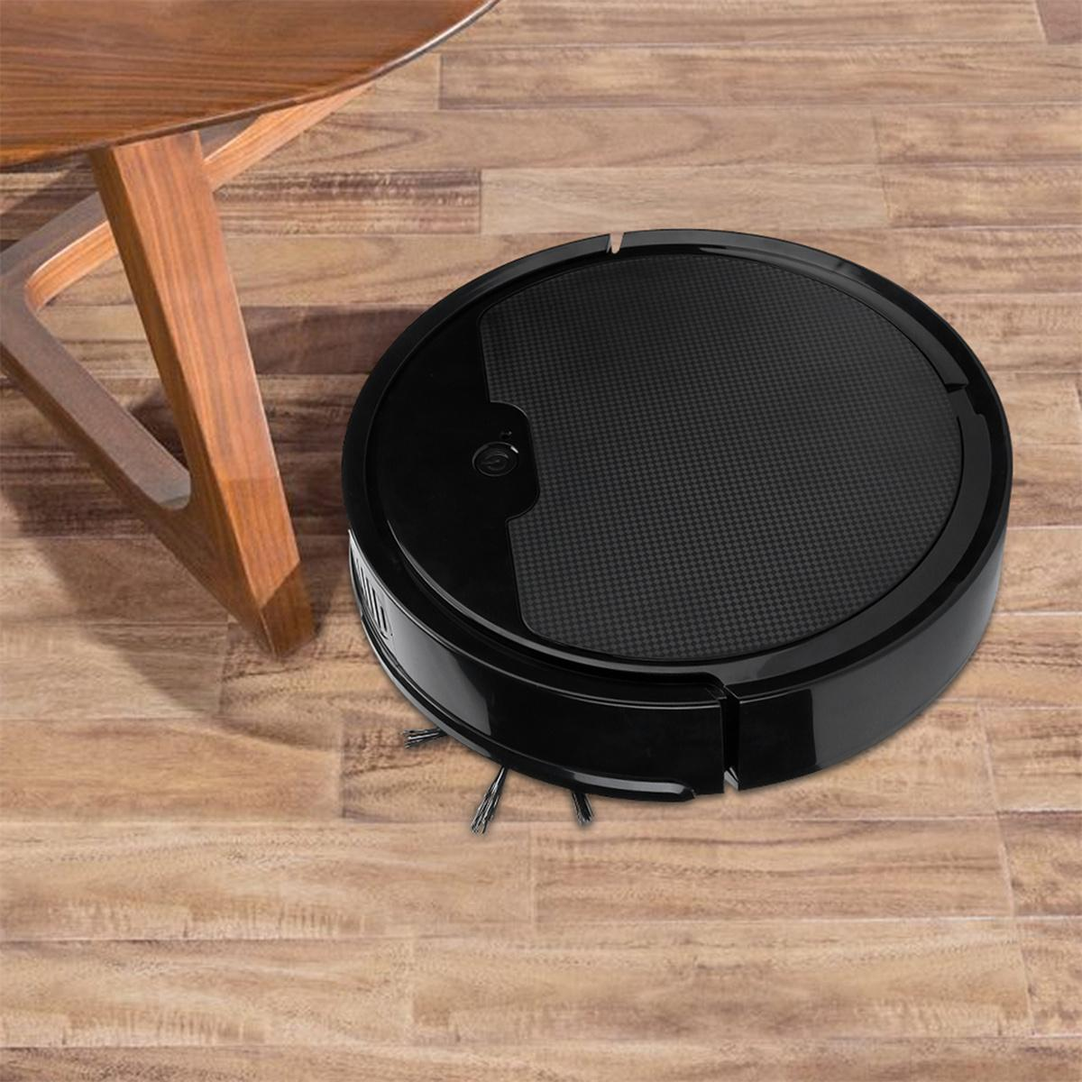 Schwarzer Roboter-Staubsauger auf Holzboden, in der Nähe eines Holztisches.
