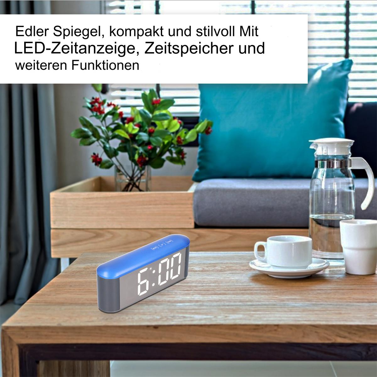 Blaue Uhr mit digitaler Anzeige, die die Zeit anzeigt, auf einem Holztisch mit Tasse und Vase.