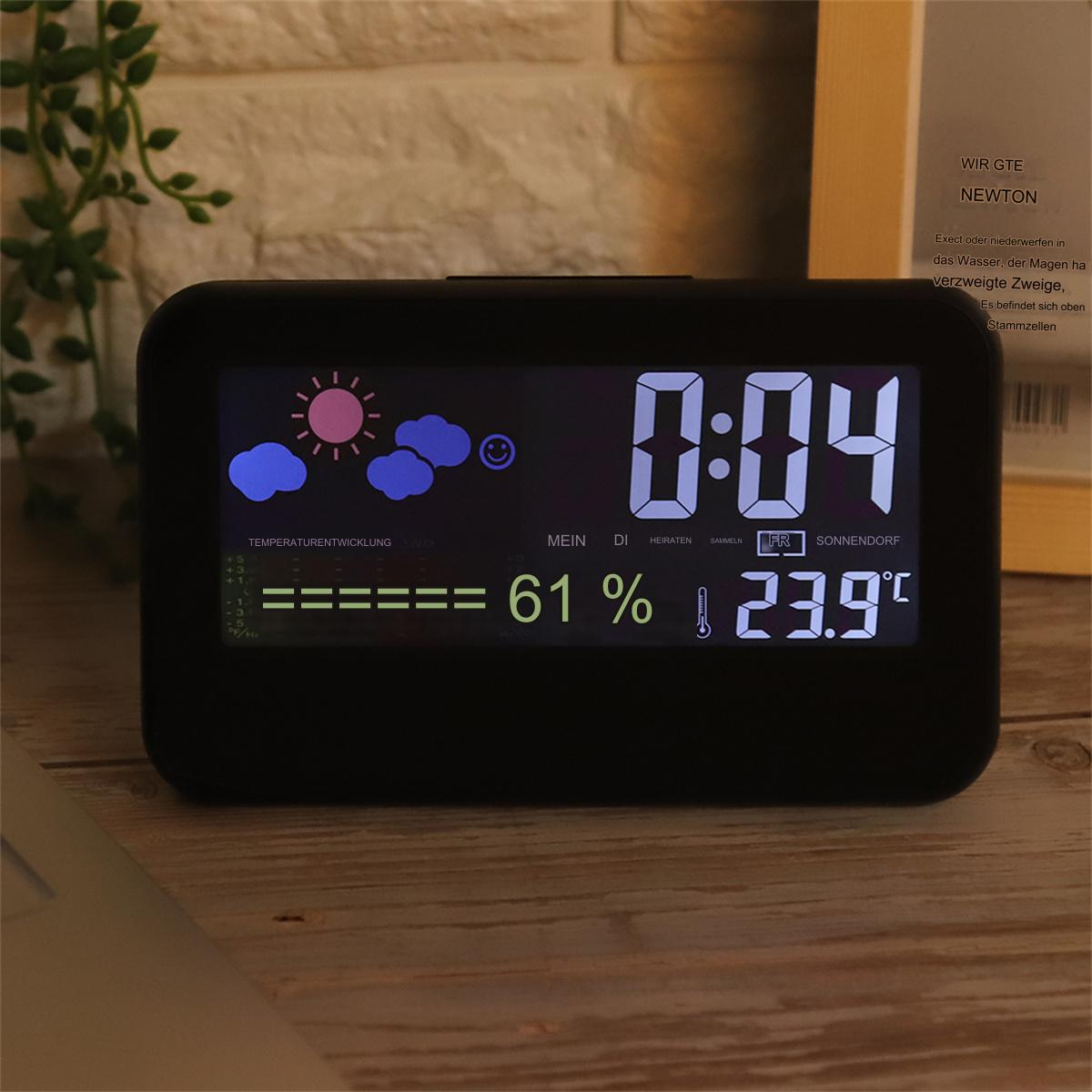 Eine schwarze Digitaluhr, die Zeit- und Wetterinformationen anzeigt, auf einer Holzoberfläche.