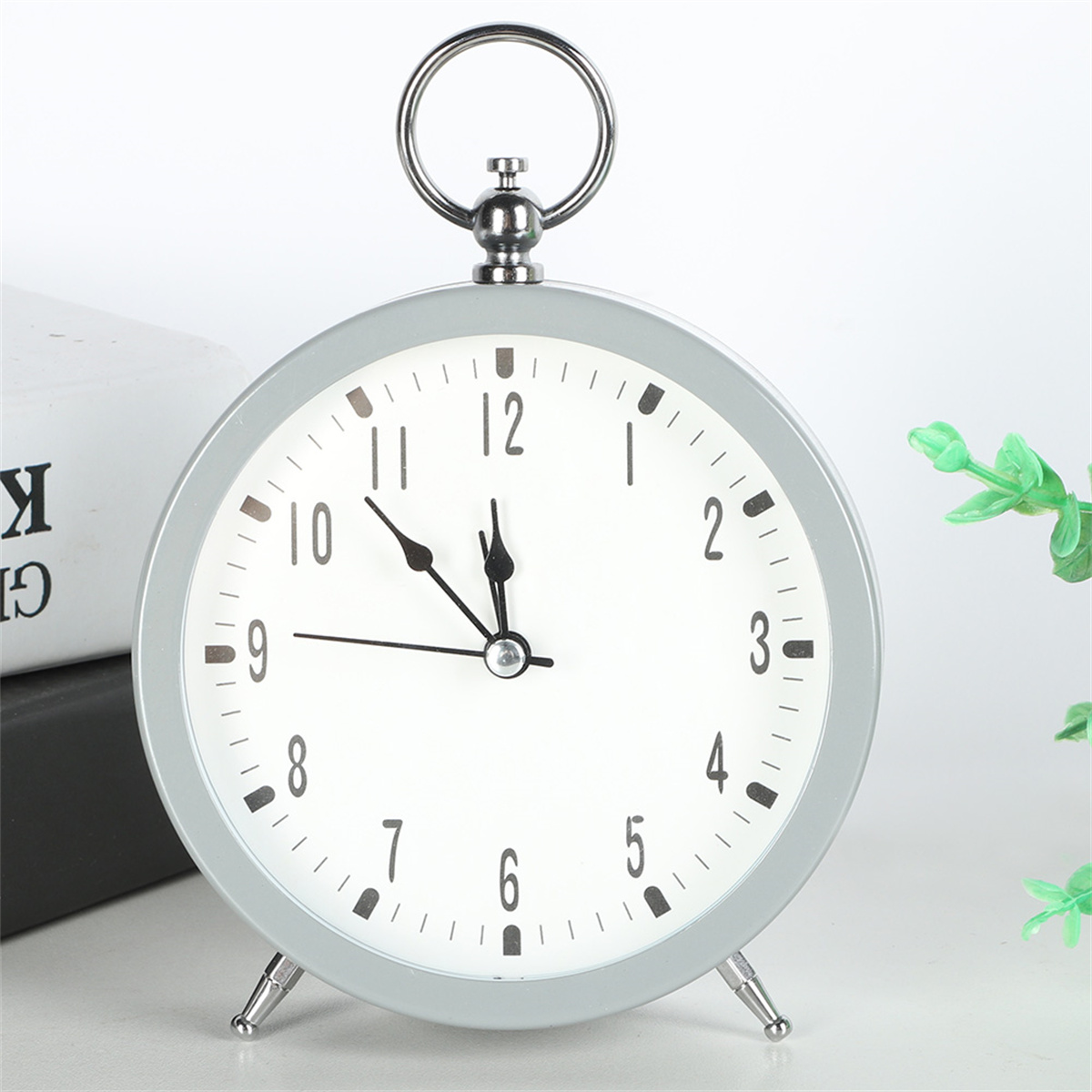Ein grauer, runder Wecker mit weißem Zifferblatt. Die Uhr zeigt 10:50 Uhr. Im Hintergrund ist etwas Grün zu sehen.