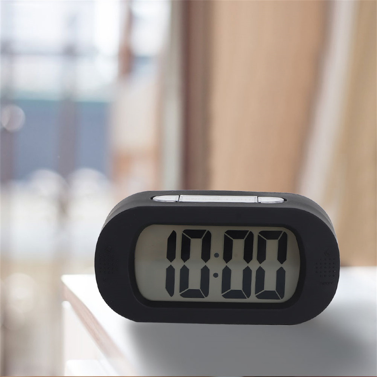 Ein schwarzer digitaler Wecker mit weißen Zahlen auf dem Display. Die Uhr steht auf einer weißen Oberfläche.