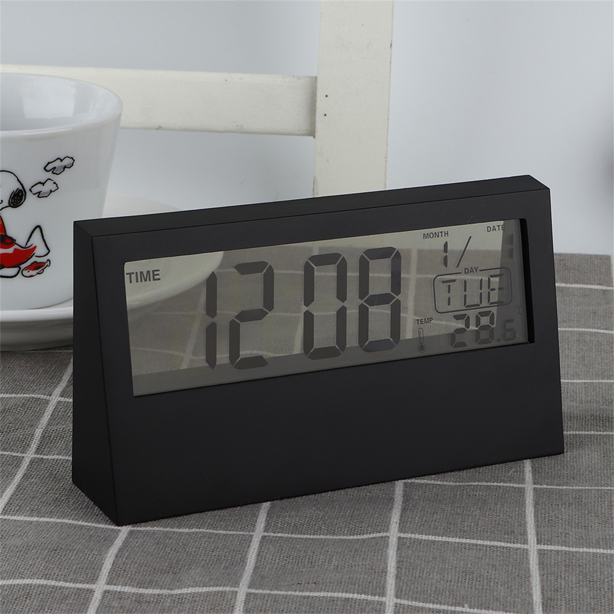 Schwarze Digitaluhr zeigt Zeit, Datum und Temperatur an. Hinter der Uhr steht eine Tasse.