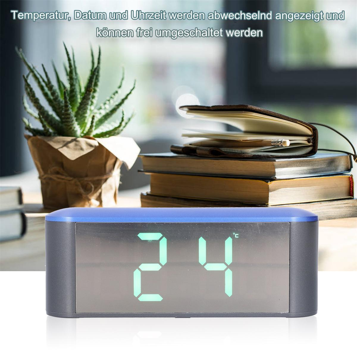 Eine Digitaluhr mit '24°C'. Eine Pflanze und Bücher dahinter auf einem Tisch. Blau-grauer Rahmen.