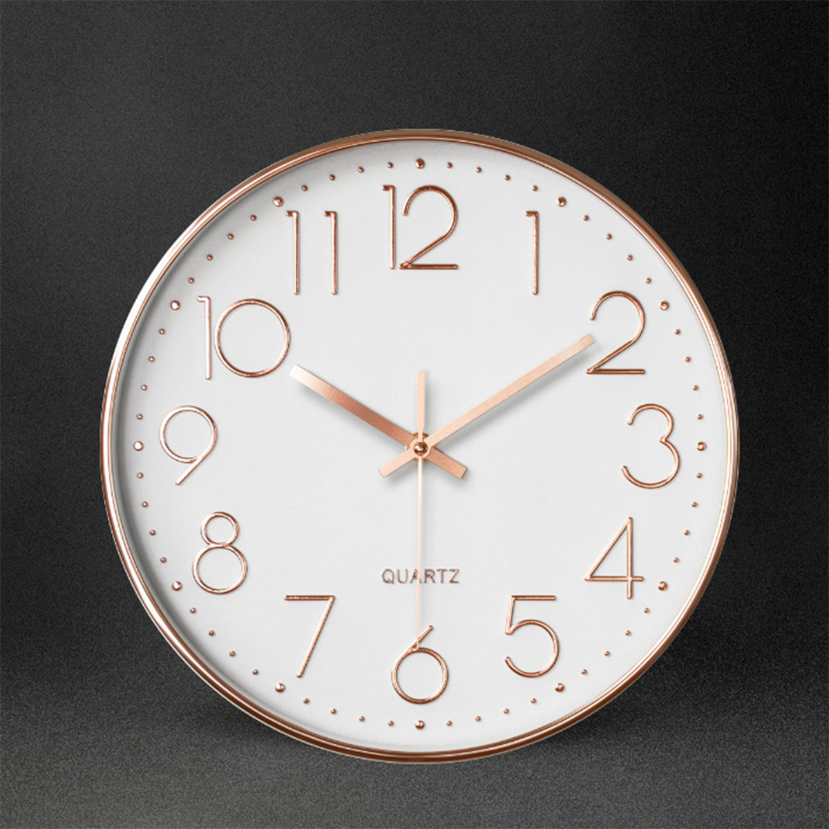 Eine runde weiße Uhr mit roségoldenen Ziffern und Zeigern auf dunkler Oberfläche.