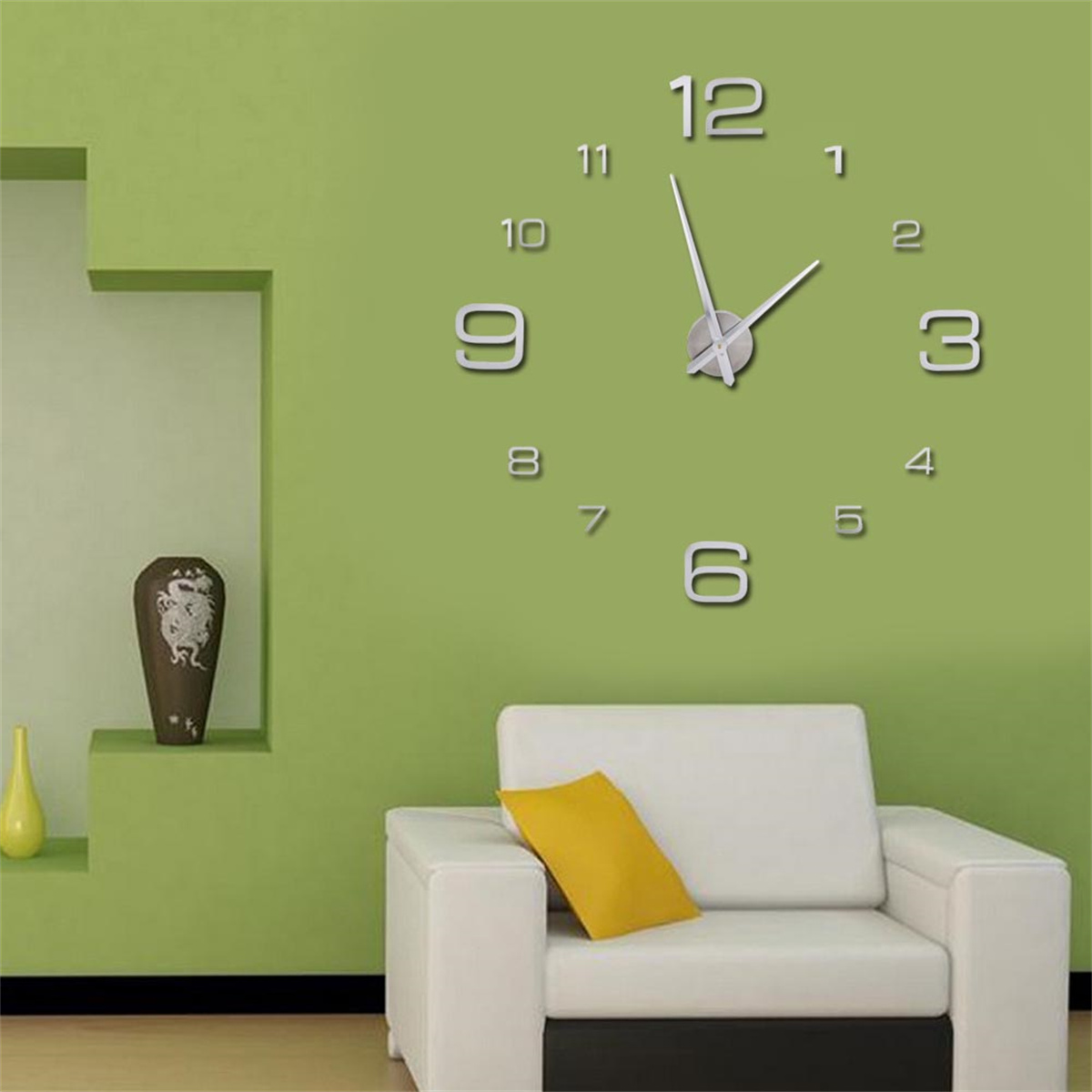 Eine Wanduhr mit silbernen Akzenten an einer grünen Wand. Ein weißes Sofa und ein gelbes Kissen.