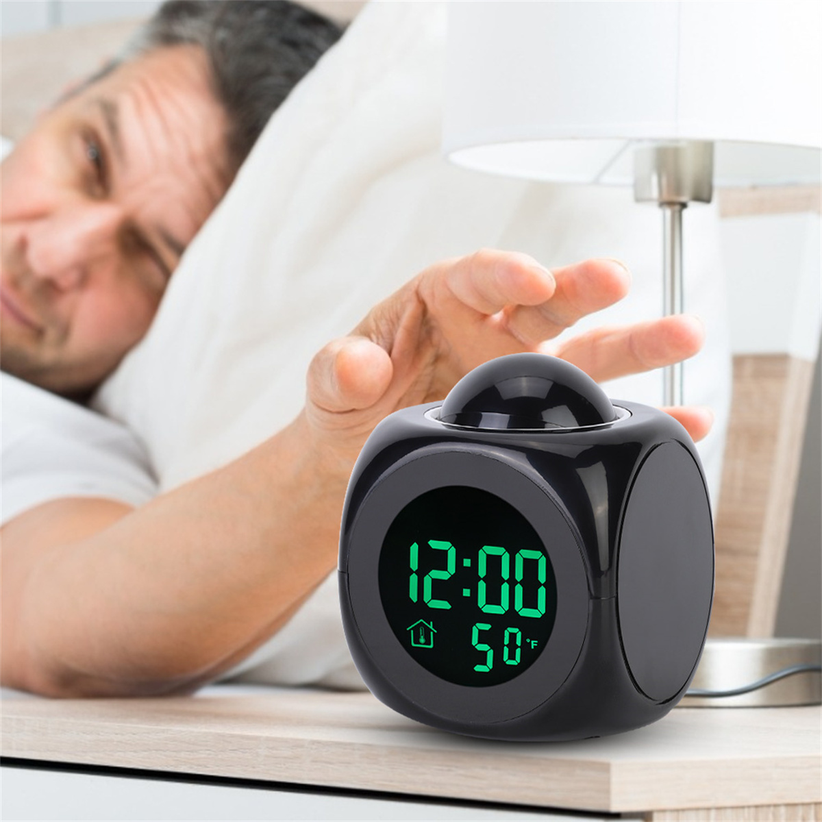 Ein Mann greift nach einem schwarzen Würfel-Wecker mit 12:00 und 50°F.