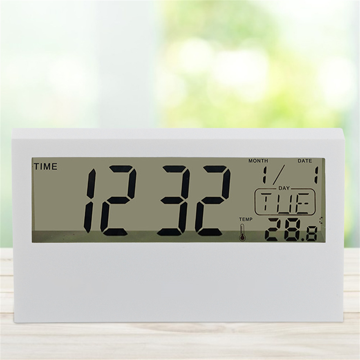 Eine weiße Digitaluhr mit der Anzeige '12:32' und dem Datum. Der Hintergrund ist verschwommen.