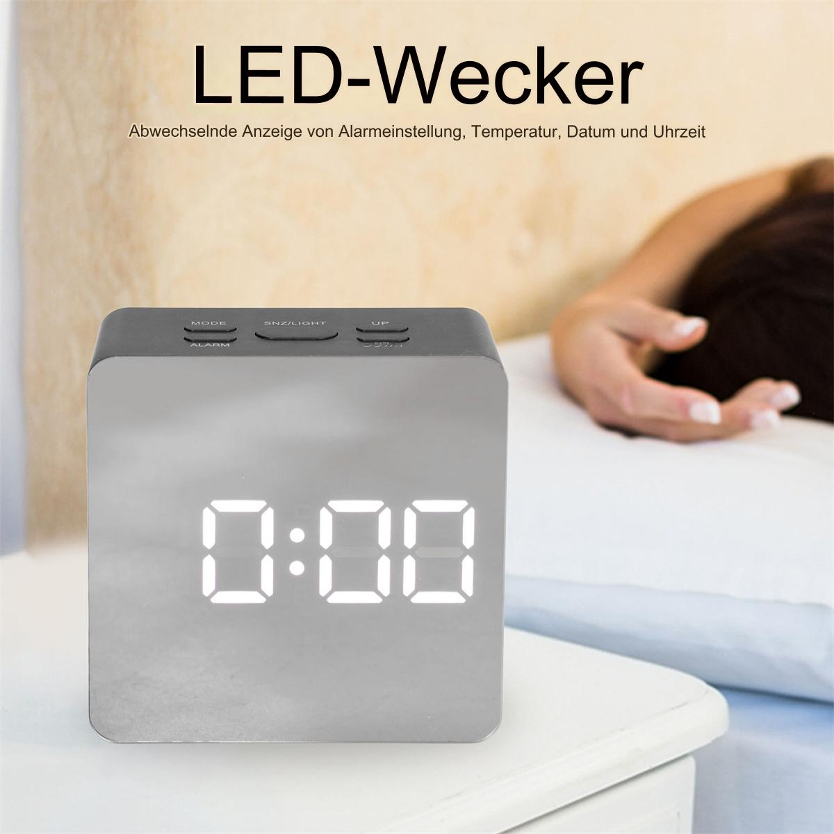 Digitaler Wecker mit der Anzeige 0:00. Die Uhr steht auf einem Tisch, im Hintergrund eine Person.
