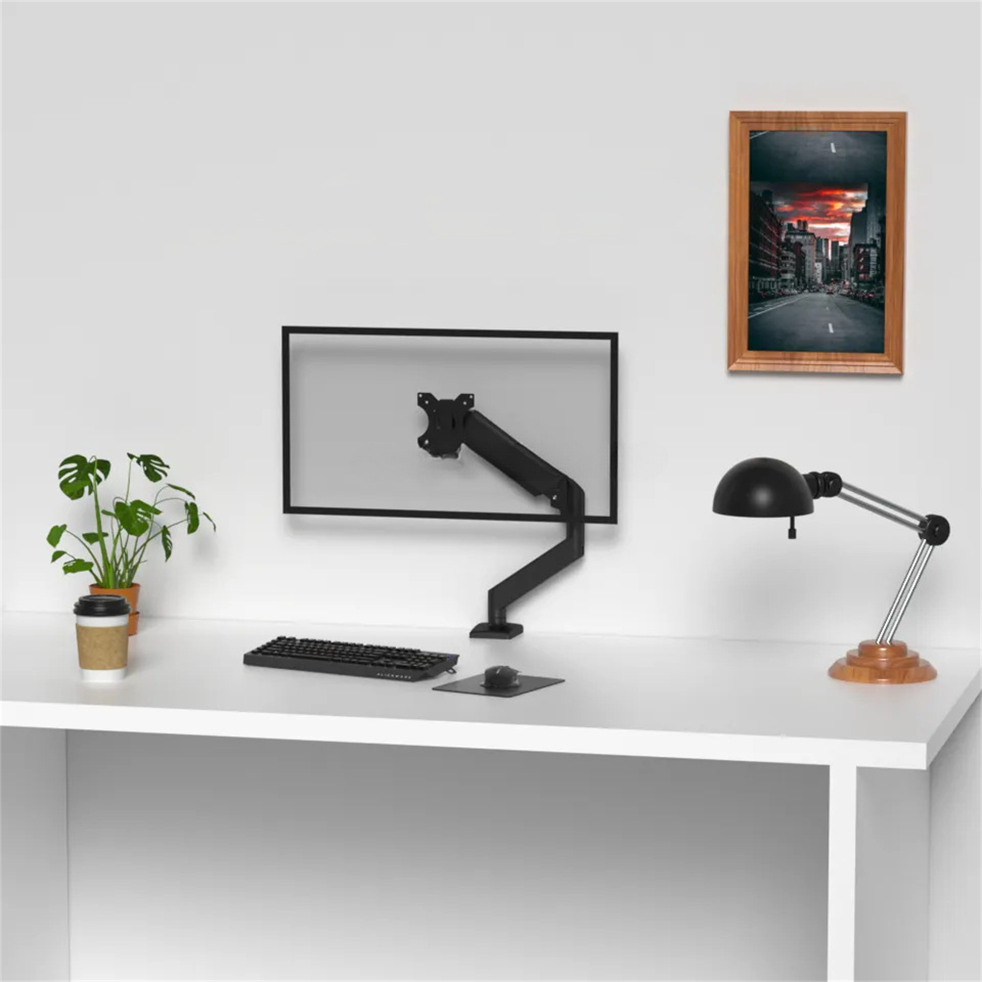 Ein Schreibtisch mit Monitor, Lampe, Tastatur und Kaffeetasse. Ein Bild an der Wand.
