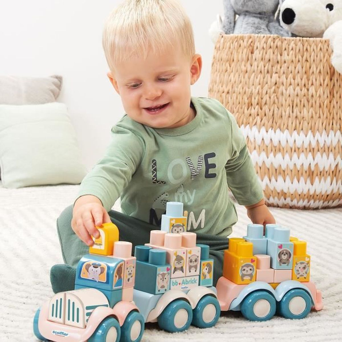 Un bambino gioca con camion giocattolo. I camion hanno blocchi con facce di animali. C'è un cesto dietro.