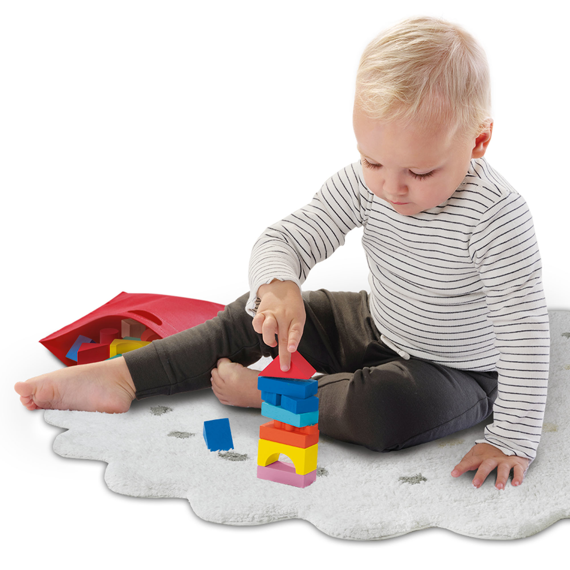 Un bambino che costruisce blocchi su un tappeto bianco. Il bambino indossa una camicia a righe e pantaloni scuri.