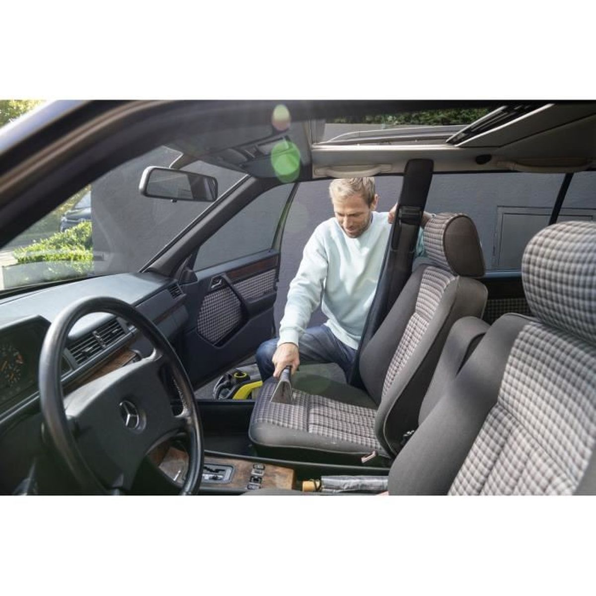 Mężczyzna czyszczący wnętrze samochodu. Używa odkurzacza na siedzeniach. Samochód jest w garażu.