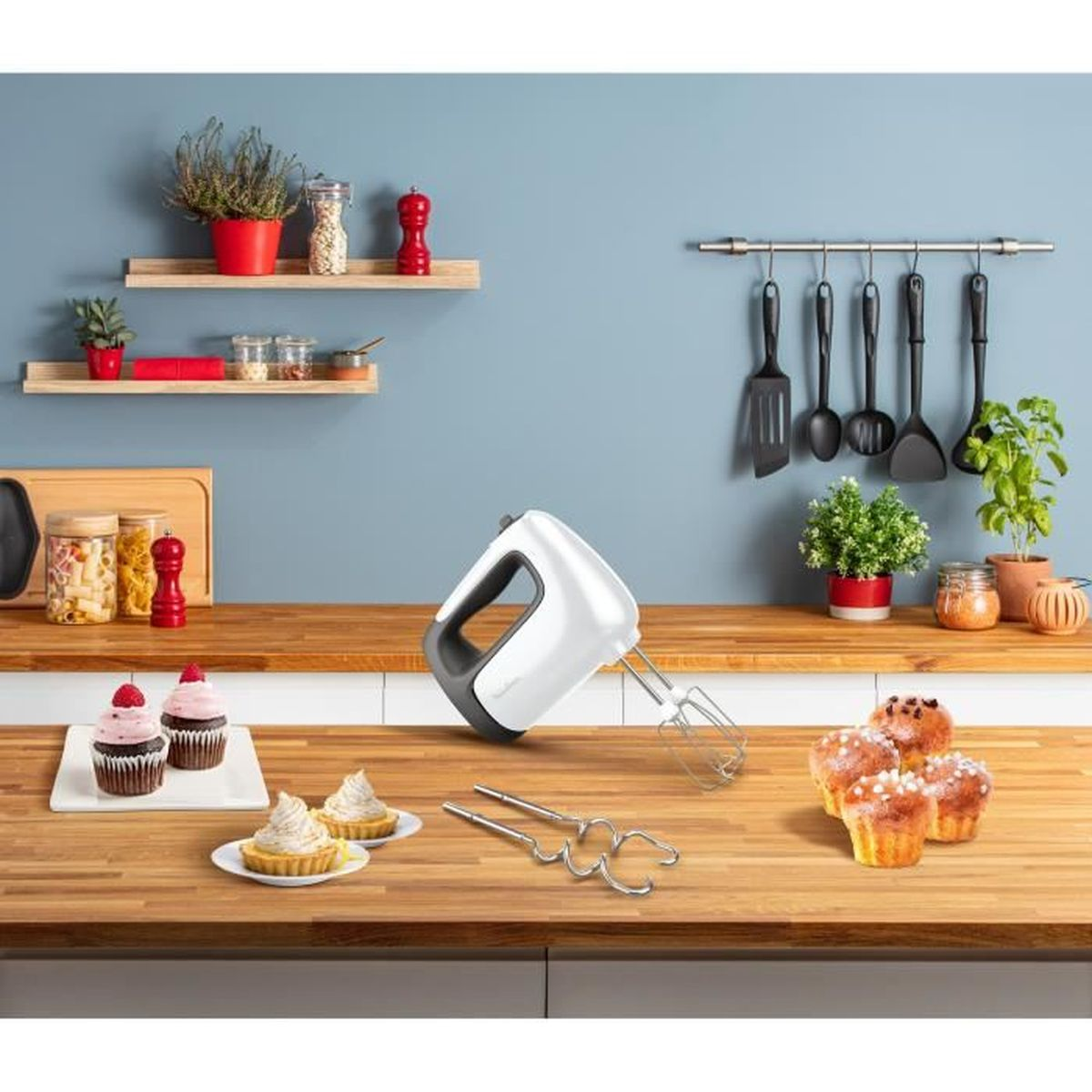 Küchentheke mit Mixer, Cupcakes und Utensilien. Hintergrund mit Regalen und Pflanzen.