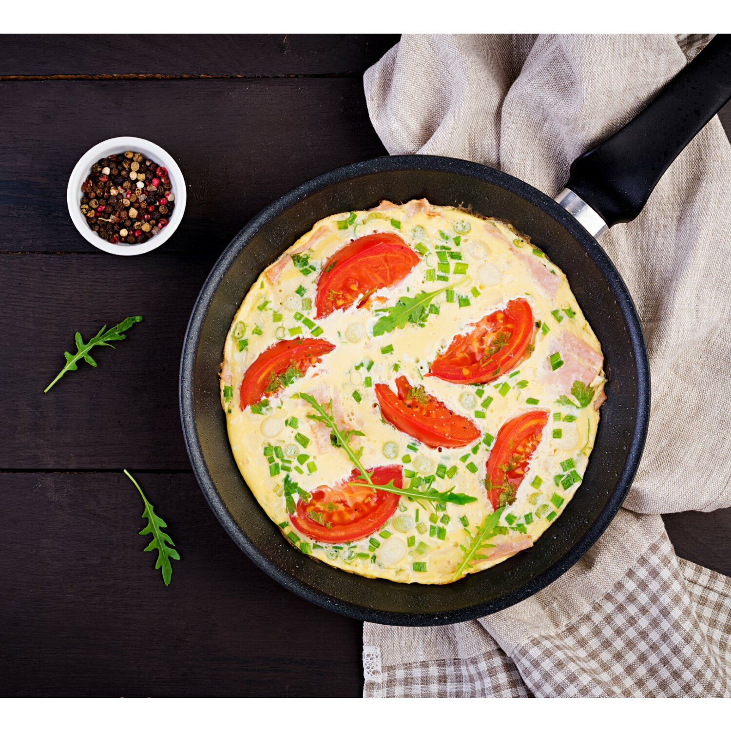 Omelett in der Pfanne mit Tomaten und Kräutern. Draufsicht auf dunkler Holzoberfläche.