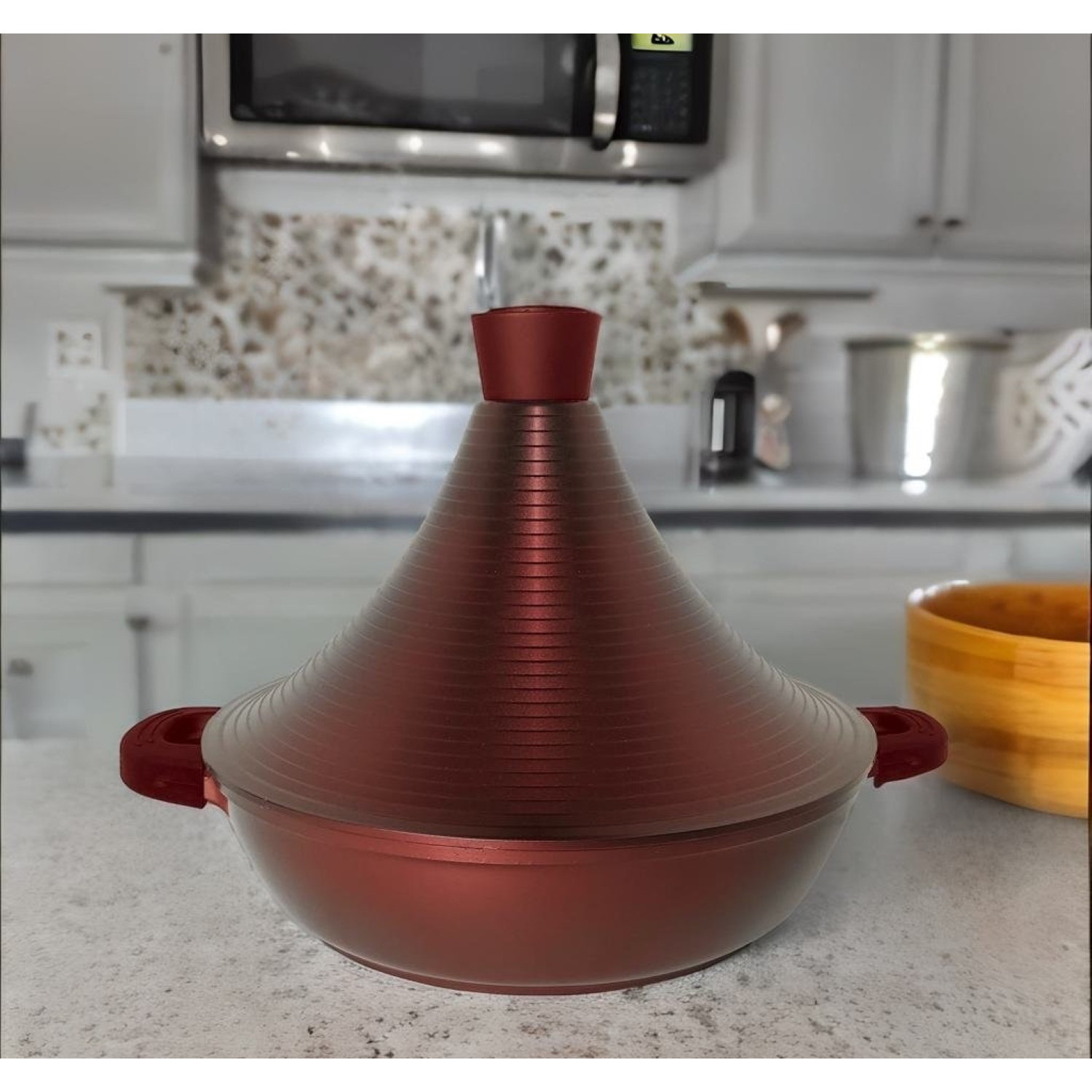 Ein roter Tajine-Topf mit konischem Deckel steht auf einer Küchenarbeitsplatte.