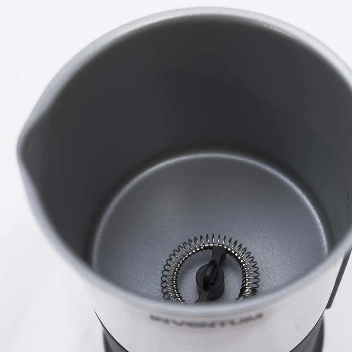 Inside of a silver milk frother. Spring coil is visible in the center.