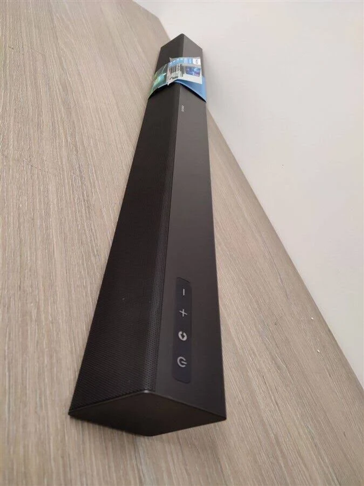 Czarny soundbar zamontowany na drewnianej powierzchni. Ma trójkątny kształt i przyciski sterowania.