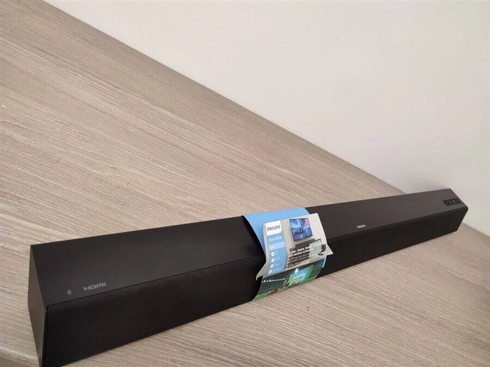 Czarny soundbar z niebieską etykietą i drewnianym tłem.