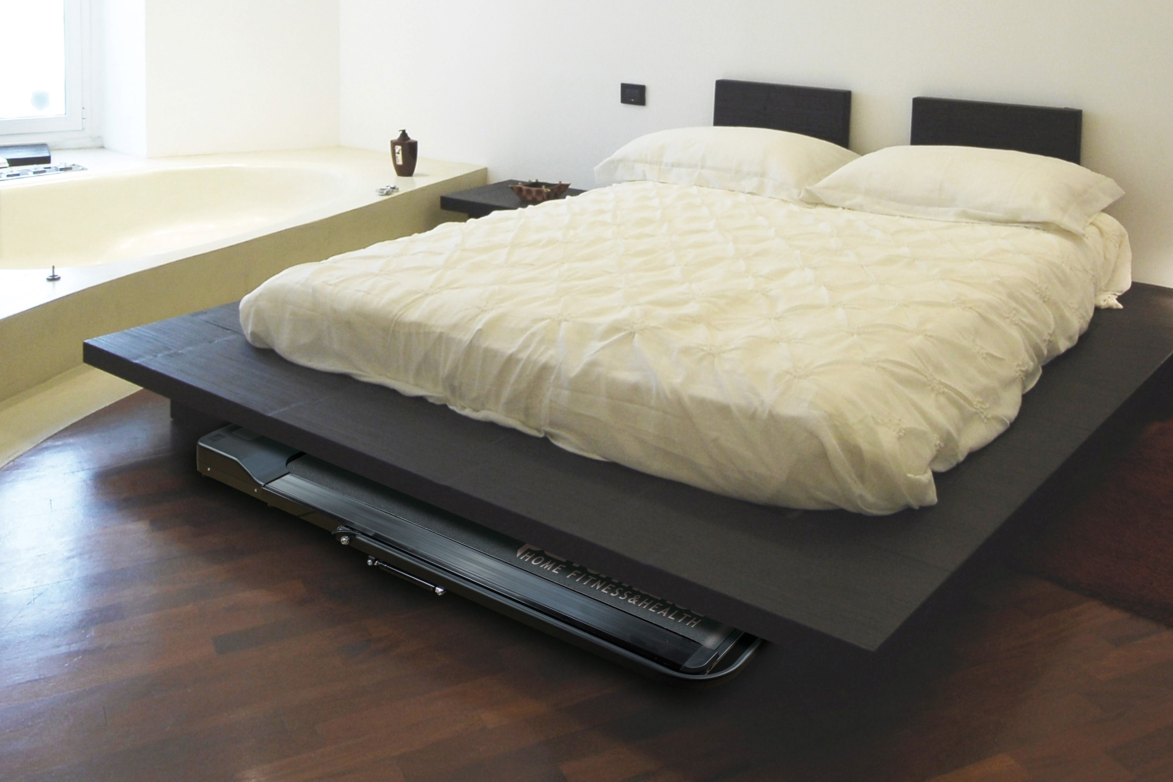 Camera da letto con letto e tapis roulant sotto. Il tapis roulant è nero, il letto è scuro.