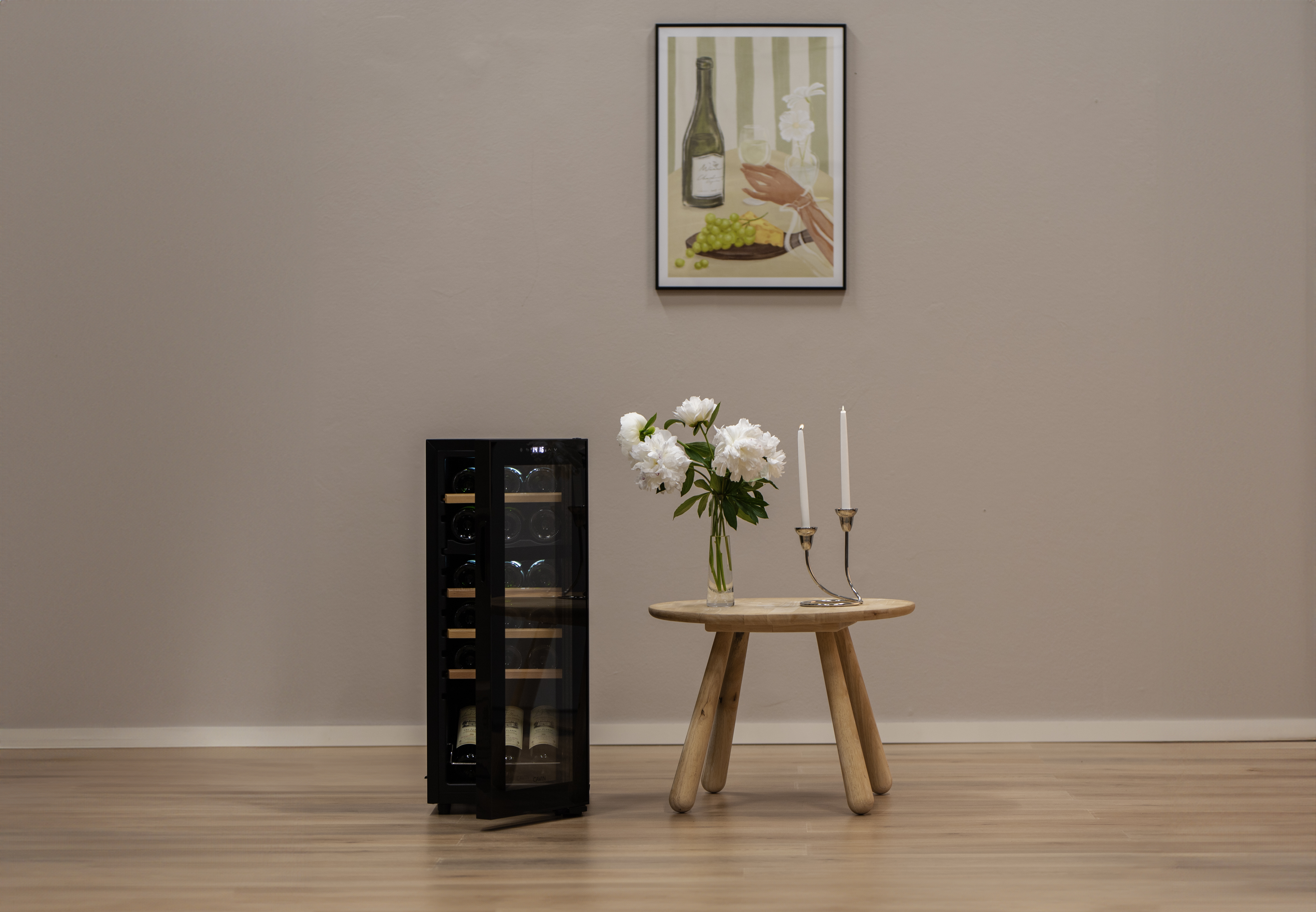 Zimmer mit Weinkühlschrank, Tisch mit Blumen und Kerzen, und Gemälde von Weinflasche und Händen.