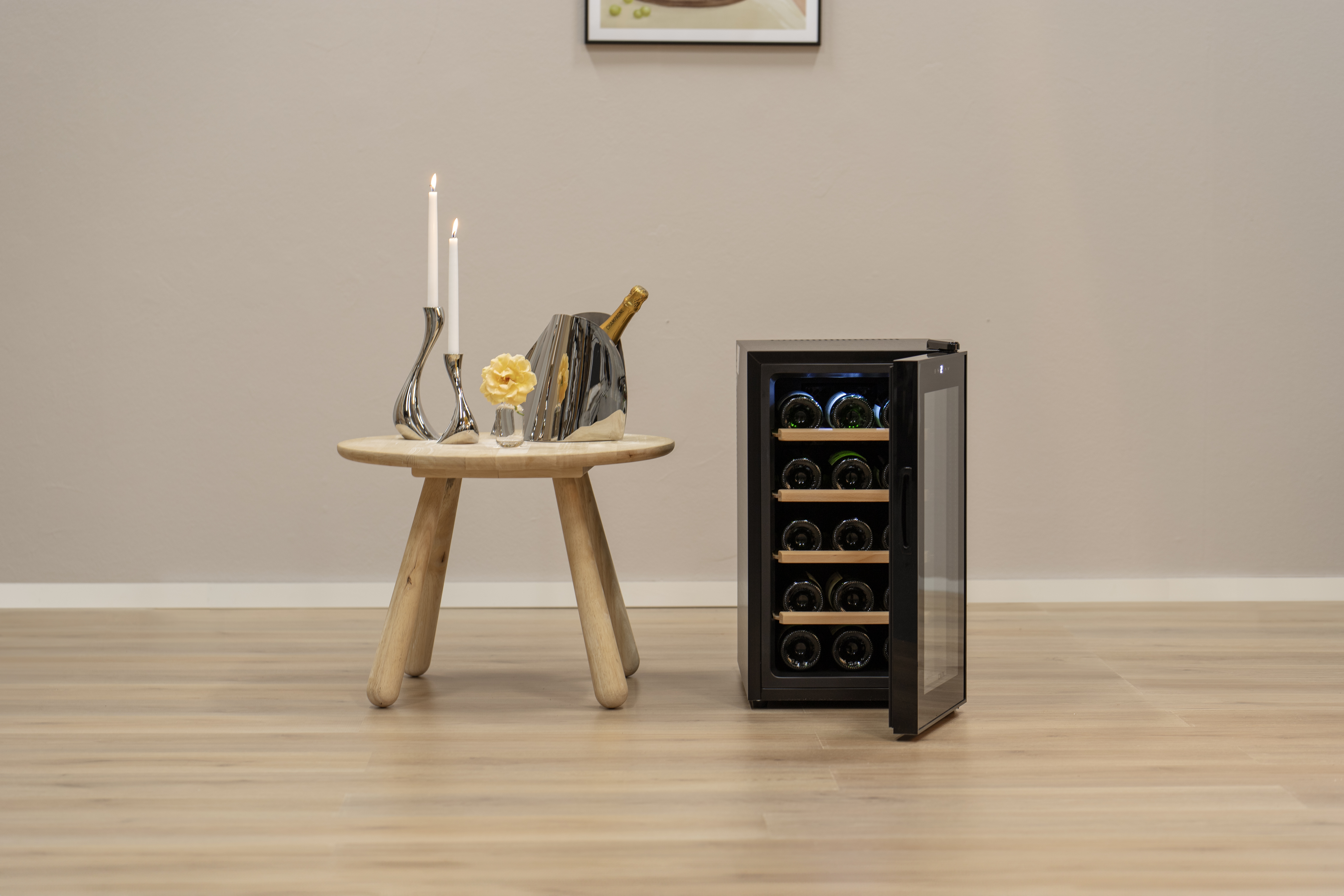 Modernes Interieur mit Weinkühler, Flaschen, Kerzen und einem kleinen Holztisch. Heller Holzfußboden und beige Wand.