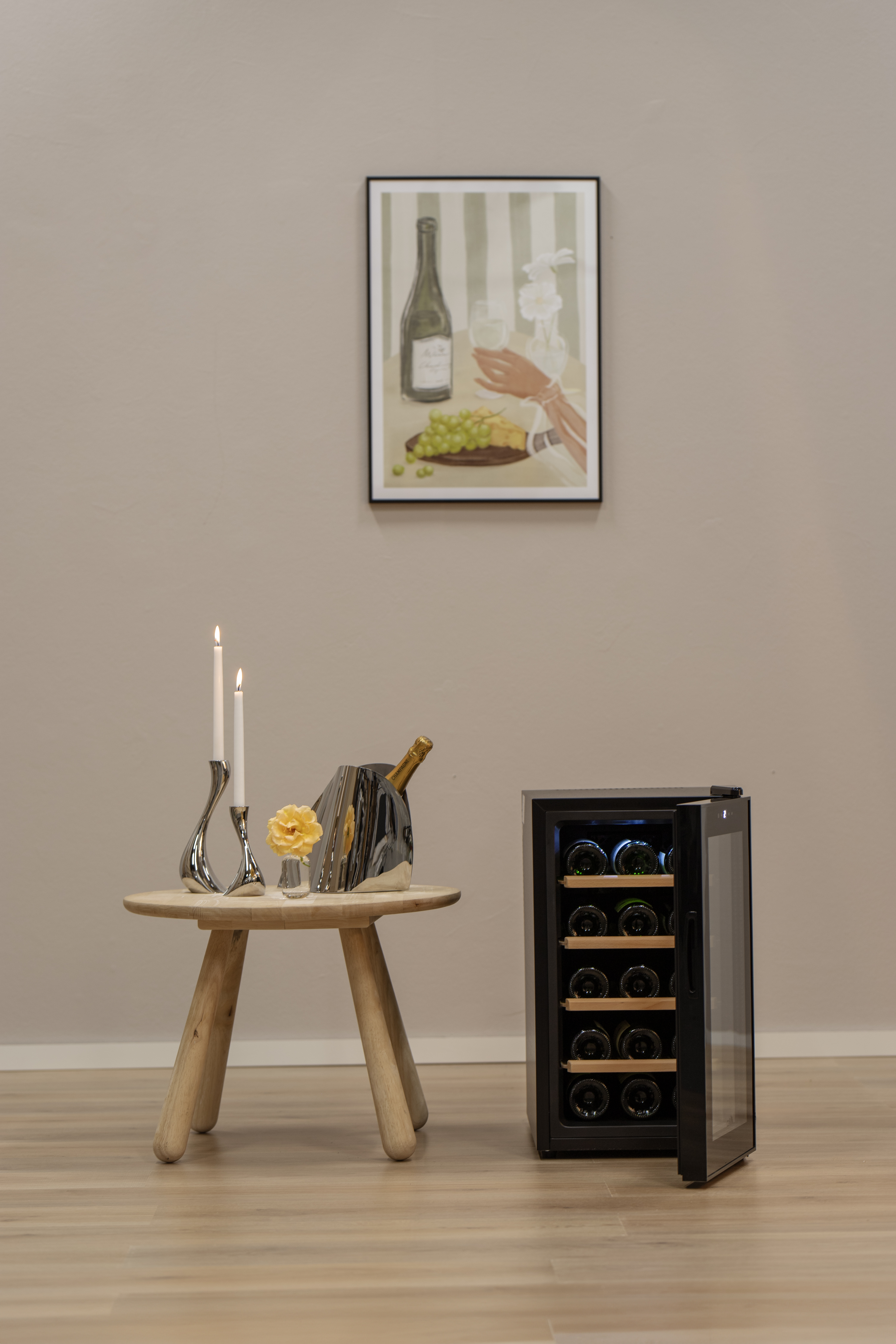 Weinflaschen, ein Weinkühler und Kerzen auf einem Tisch. Ein Bild hängt an der Wand.