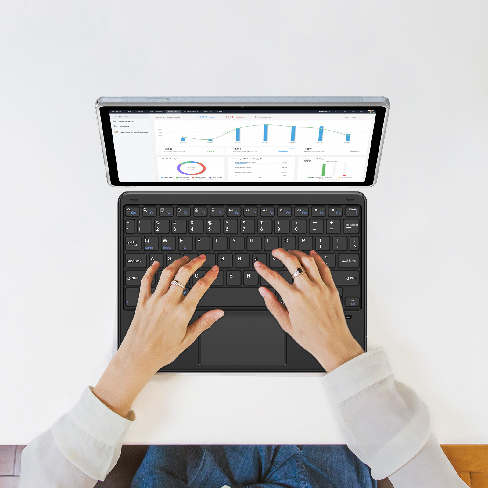 Una persona usando un teclado negro con un panel táctil, con una tableta mostrando un gráfico encima.