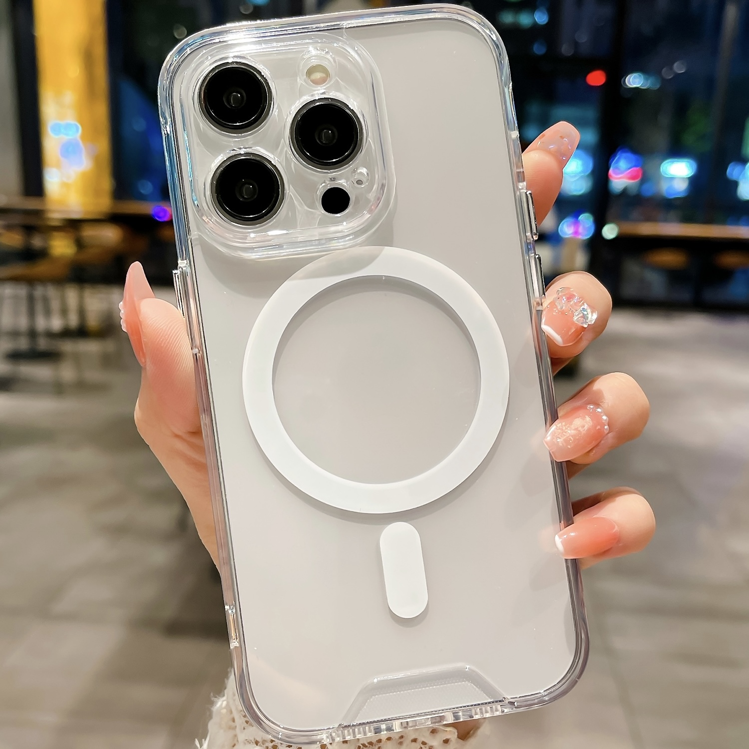 Hand hält Telefon mit durchsichtiger Hülle und weißem MagSafe-Ring.