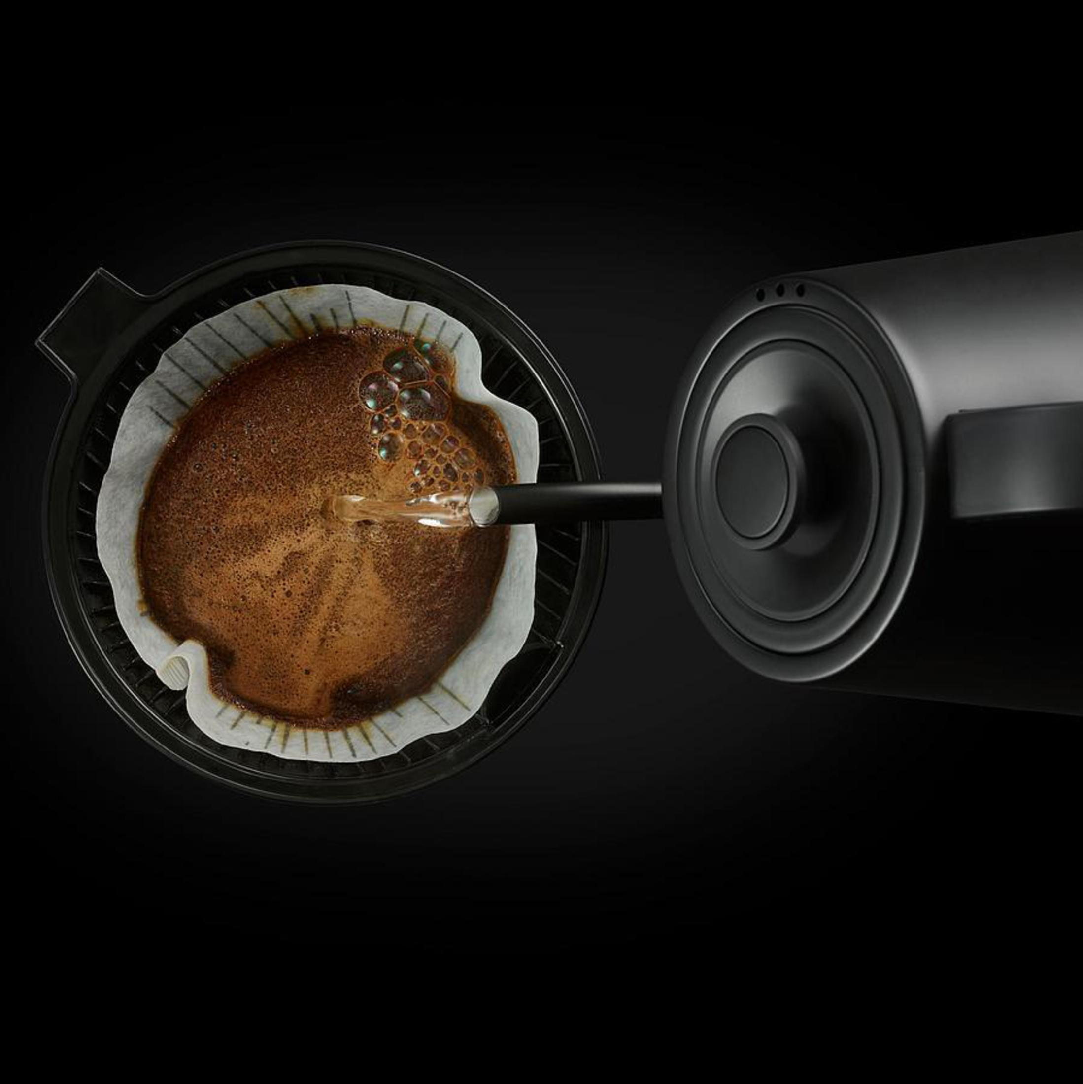 Kaffeezubereitung: Wasser gießt in einen Filter mit Kaffeepulver in dunkler Umgebung.