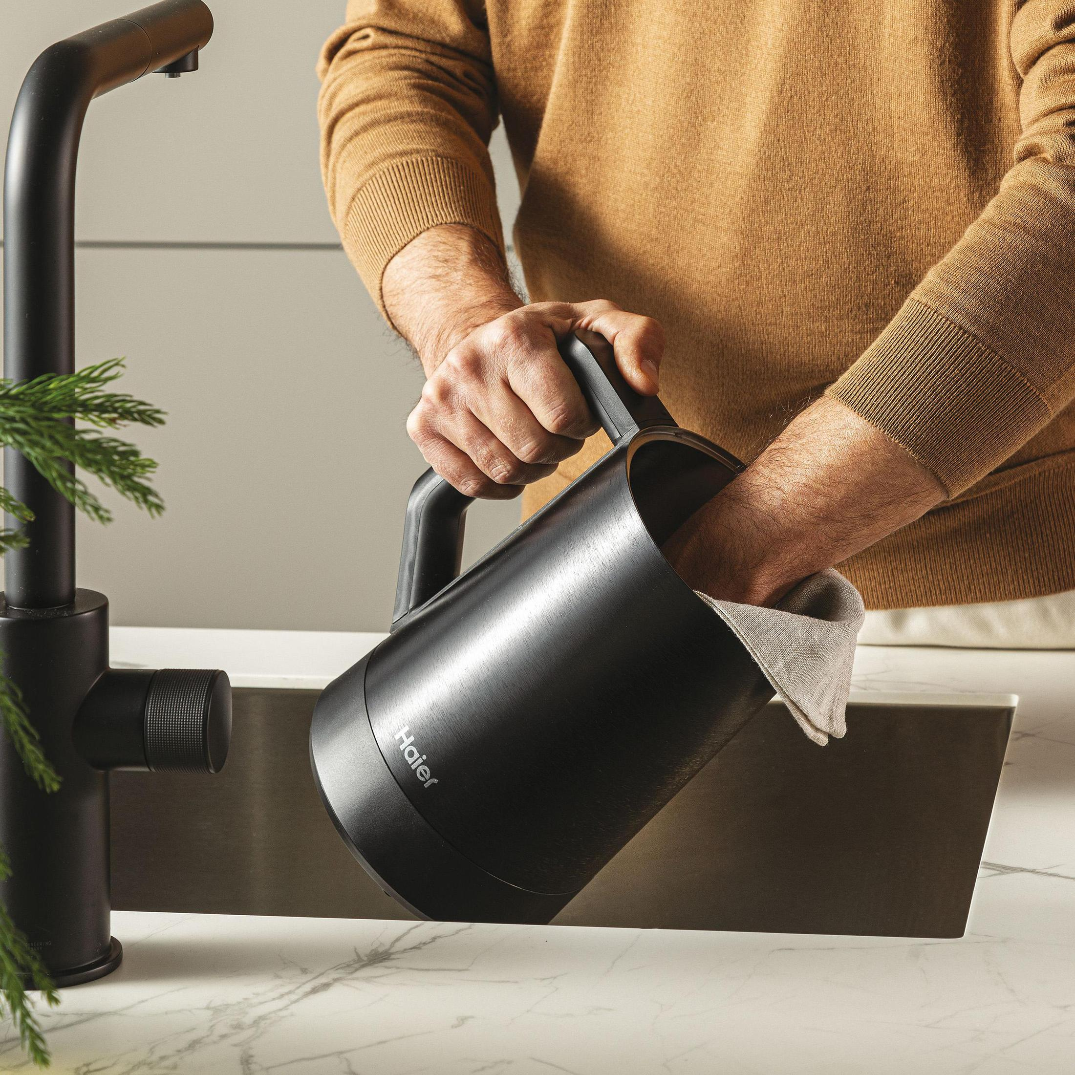 Osoba myjąca czarny czajnik w zlewozmywaku kuchennym. Czarna bateria i marmurowy blat obecne.