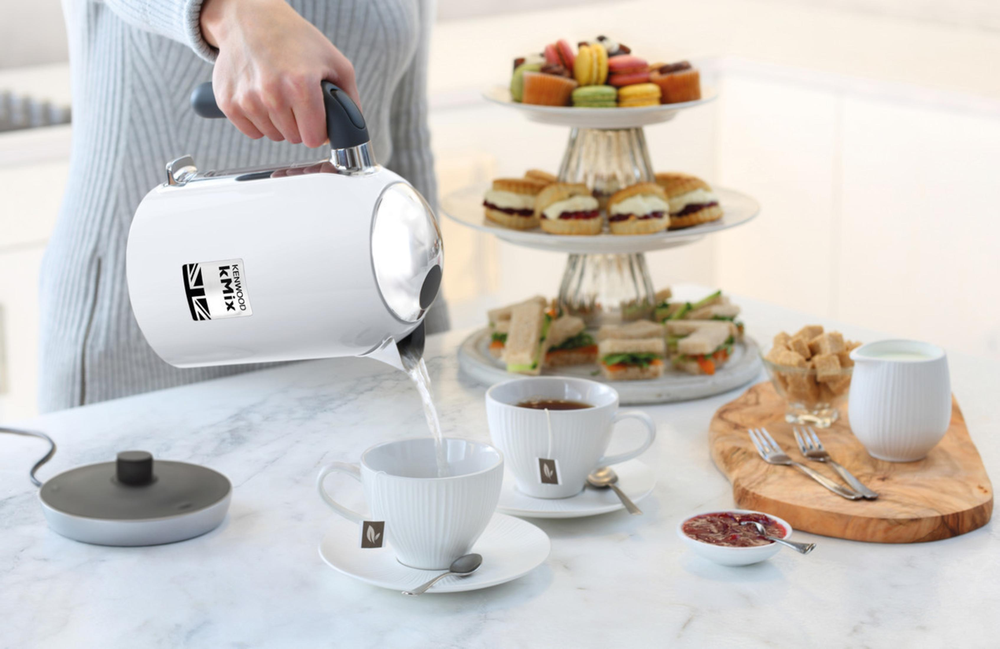 Person gießt heißes Wasser aus einem weißen Wasserkocher in eine Tasse. Tee-Setting.