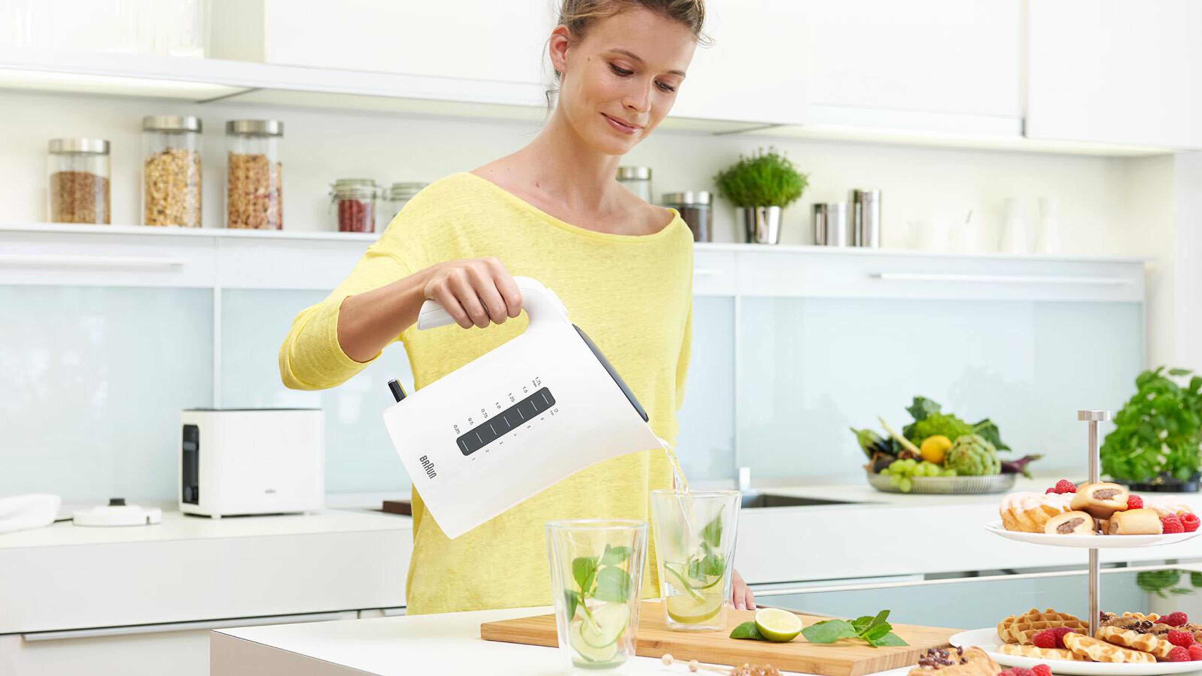 Kobieta nalewa wodę z białego czajnika do szklanek z miętą i limonką w kuchni.