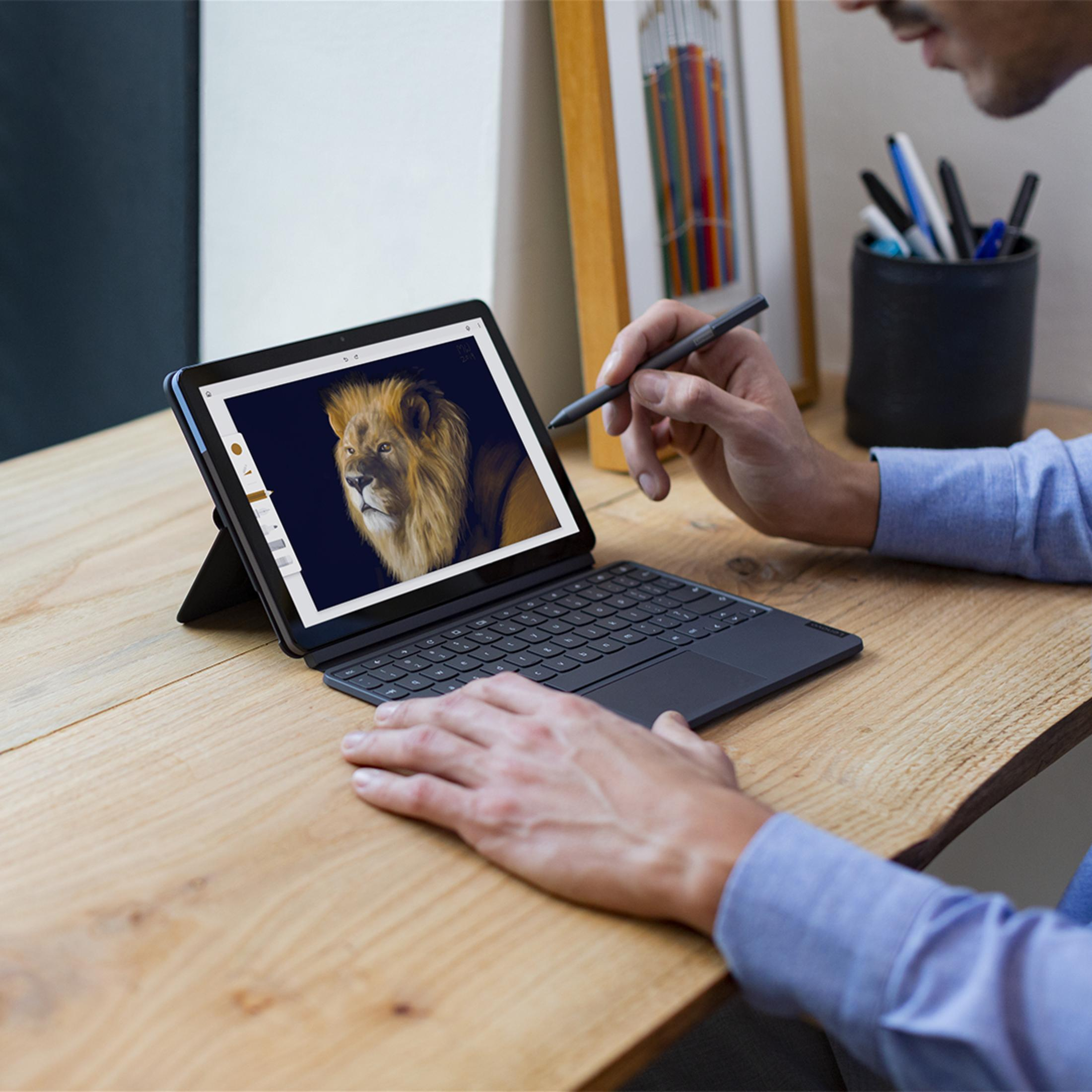 Eine Person zeichnet mit einem Tablet und Tastatur einen Löwen. Weitere Gegenstände auf dem Schreibtisch.