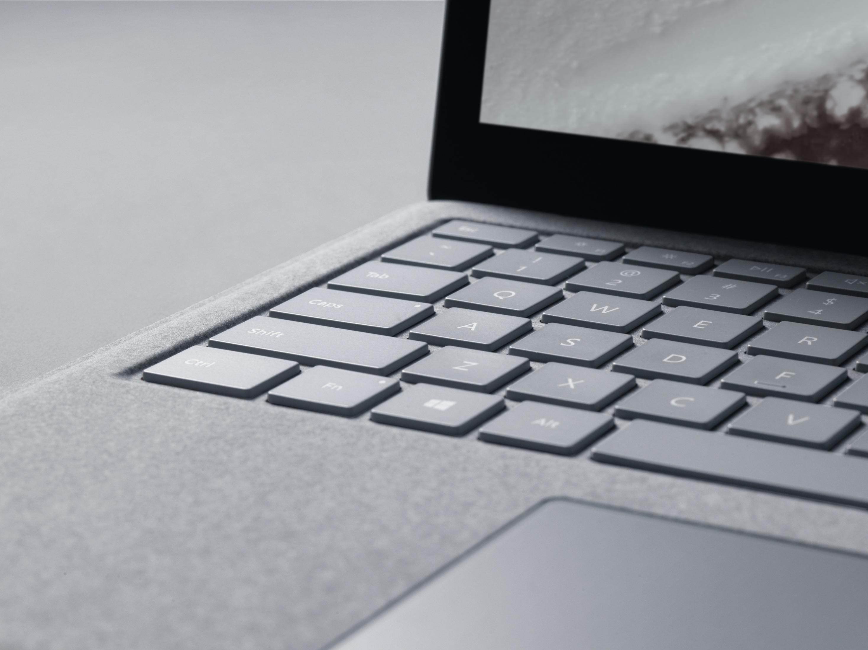 Nahaufnahme einer Laptop-Tastatur. Tasten sind grau mit weißen Buchstaben. Der Bildschirm zeigt eine verschneite Landschaft.