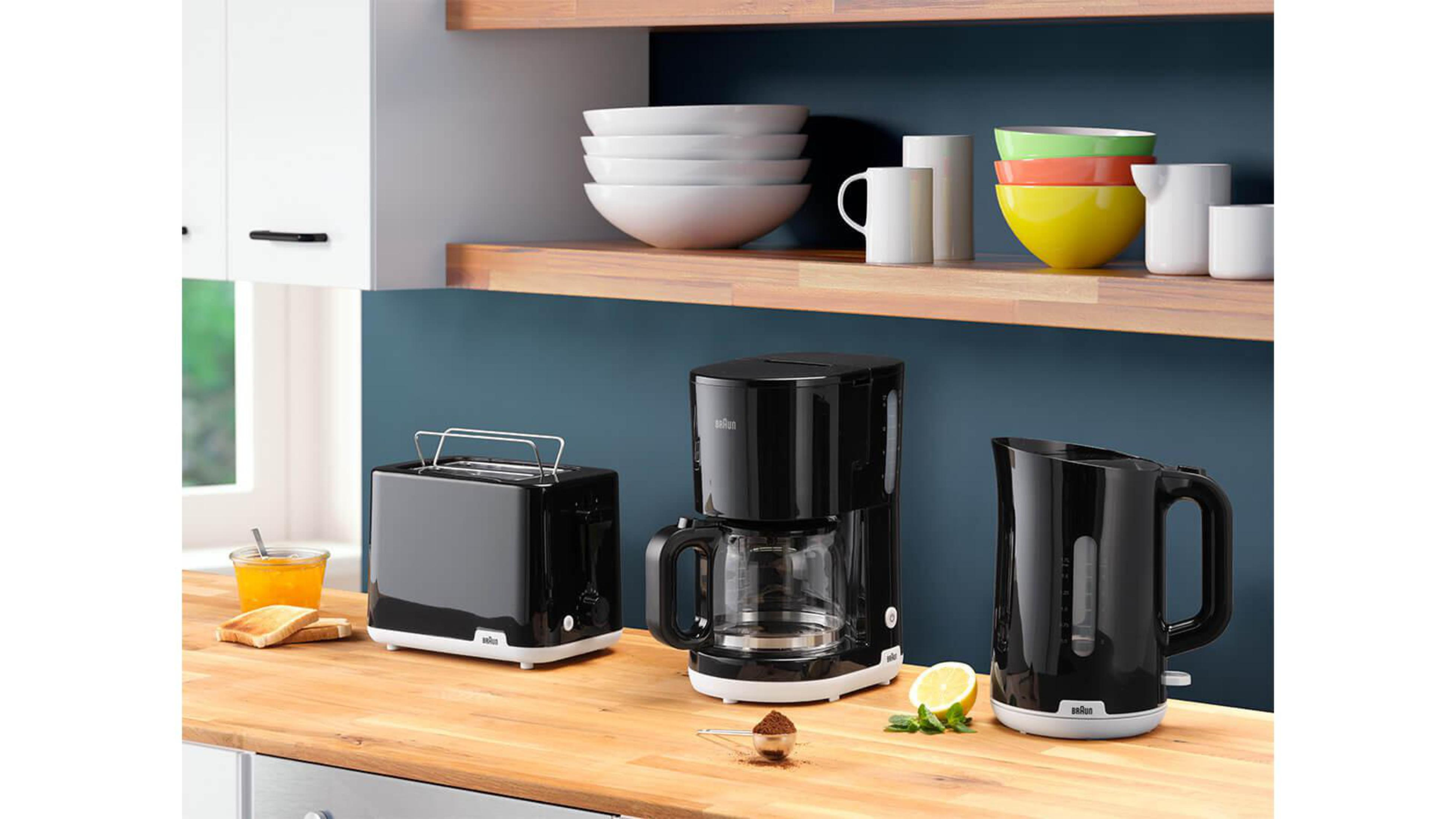 Blat kuchenny z tosterem, ekspresem do kawy, czajnikiem, miskami i kubkami, z artykułami spożywczymi.