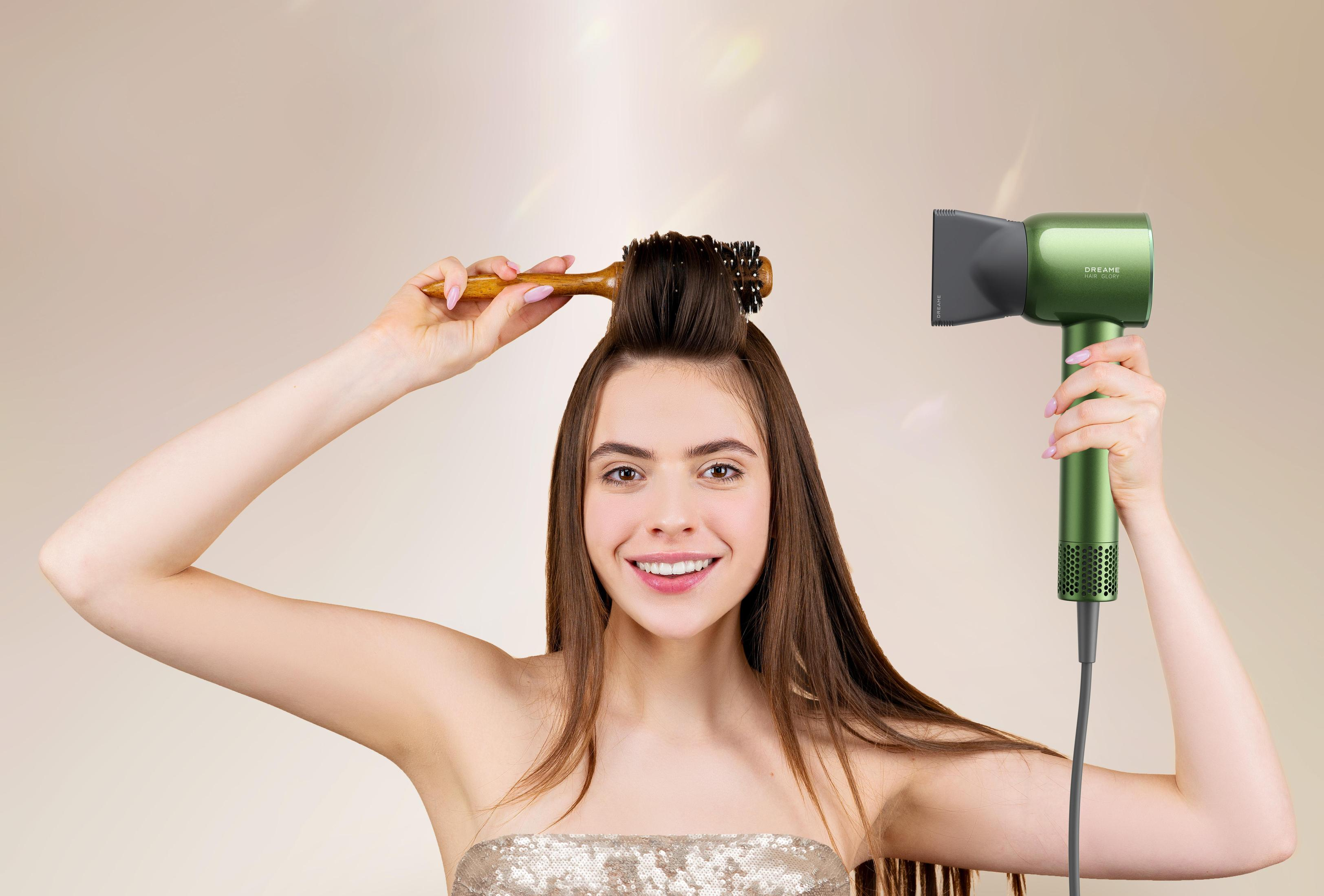 Eine Frau hält eine Haarbürste und einen grünen Haartrockner, lächelt, mit hochgestyltem Haar.