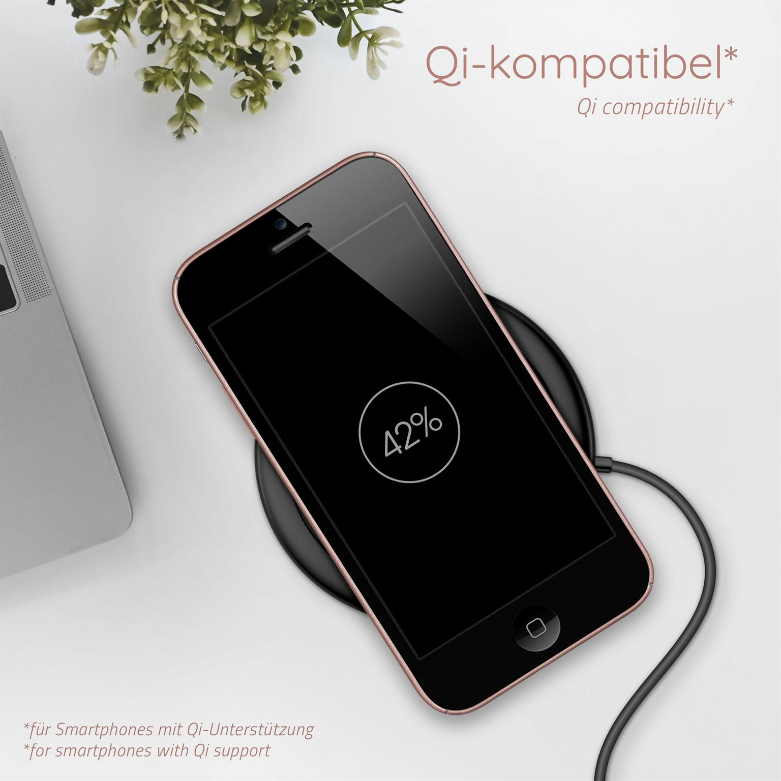 Rosafarbenes Telefon auf kabellosem Ladegerät mit 42 % Ladeanzeige. Weißer Hintergrund mit Pflanze und Laptop.