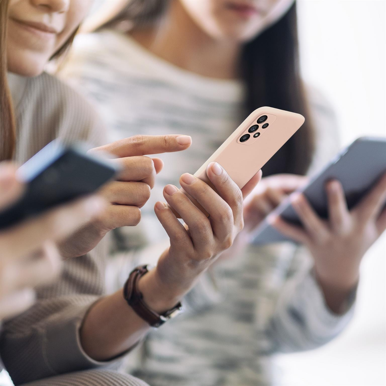 Drei Personen halten Telefone und schauen auf ihre Bildschirme, ein Telefon ist rosa.